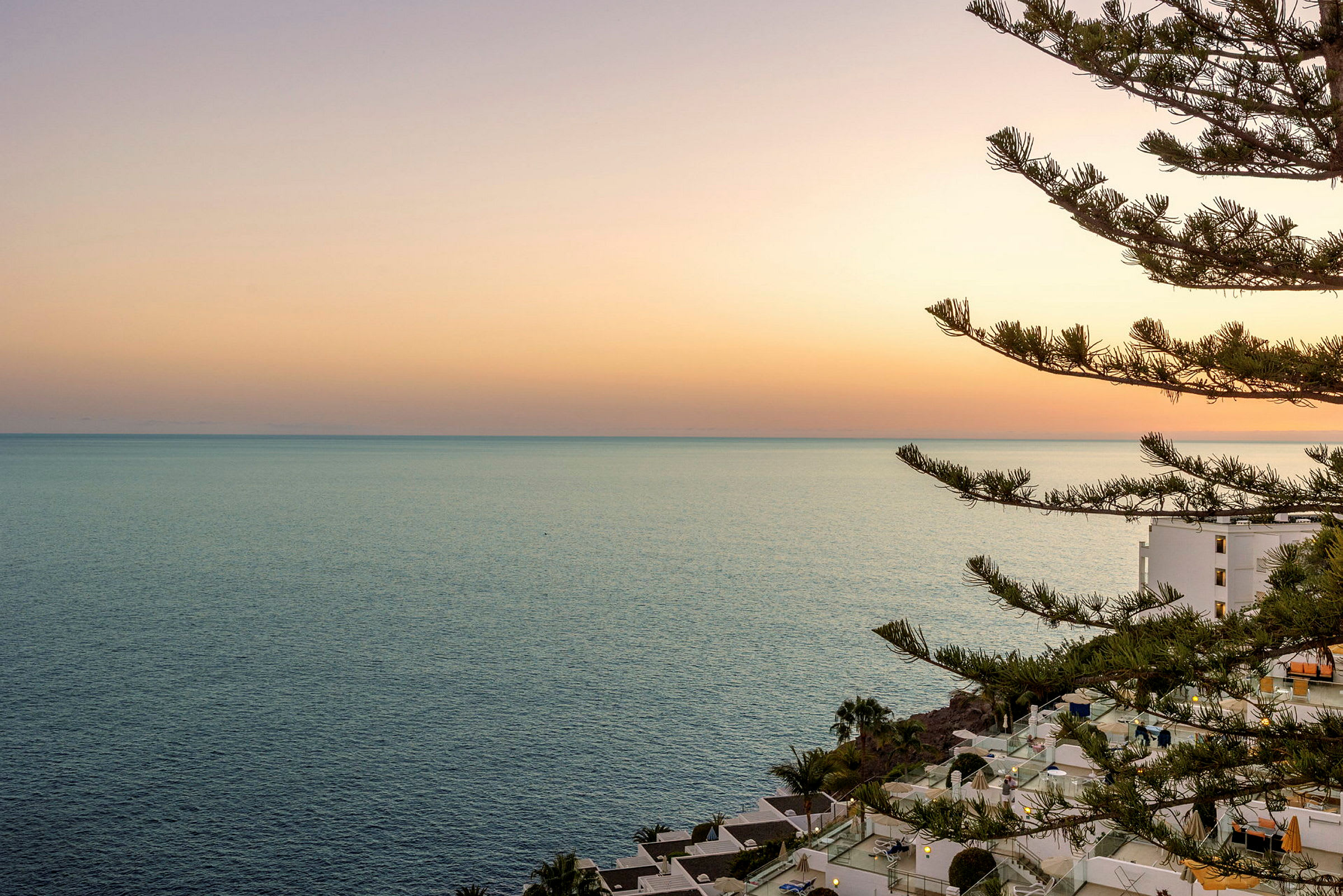 Solnedgang over havet med en bygning og træer i forgrunden. (AI-genereret tekst)