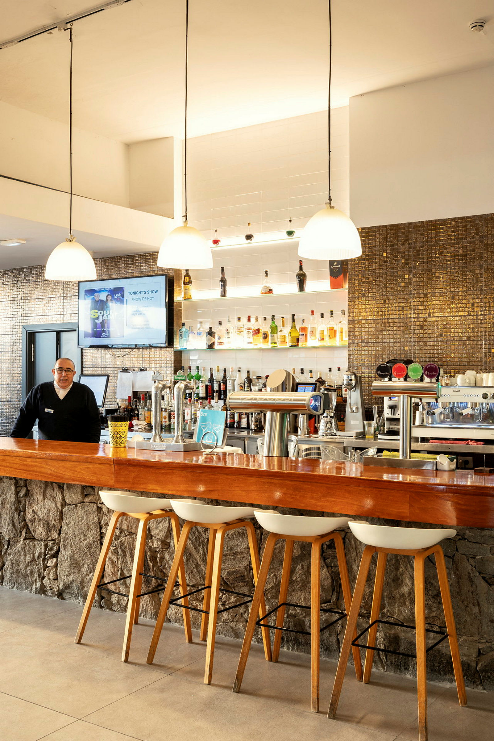 En hotelbar med træbord og stole samt hylder fyldt med flasker. (AI-genereret tekst)
