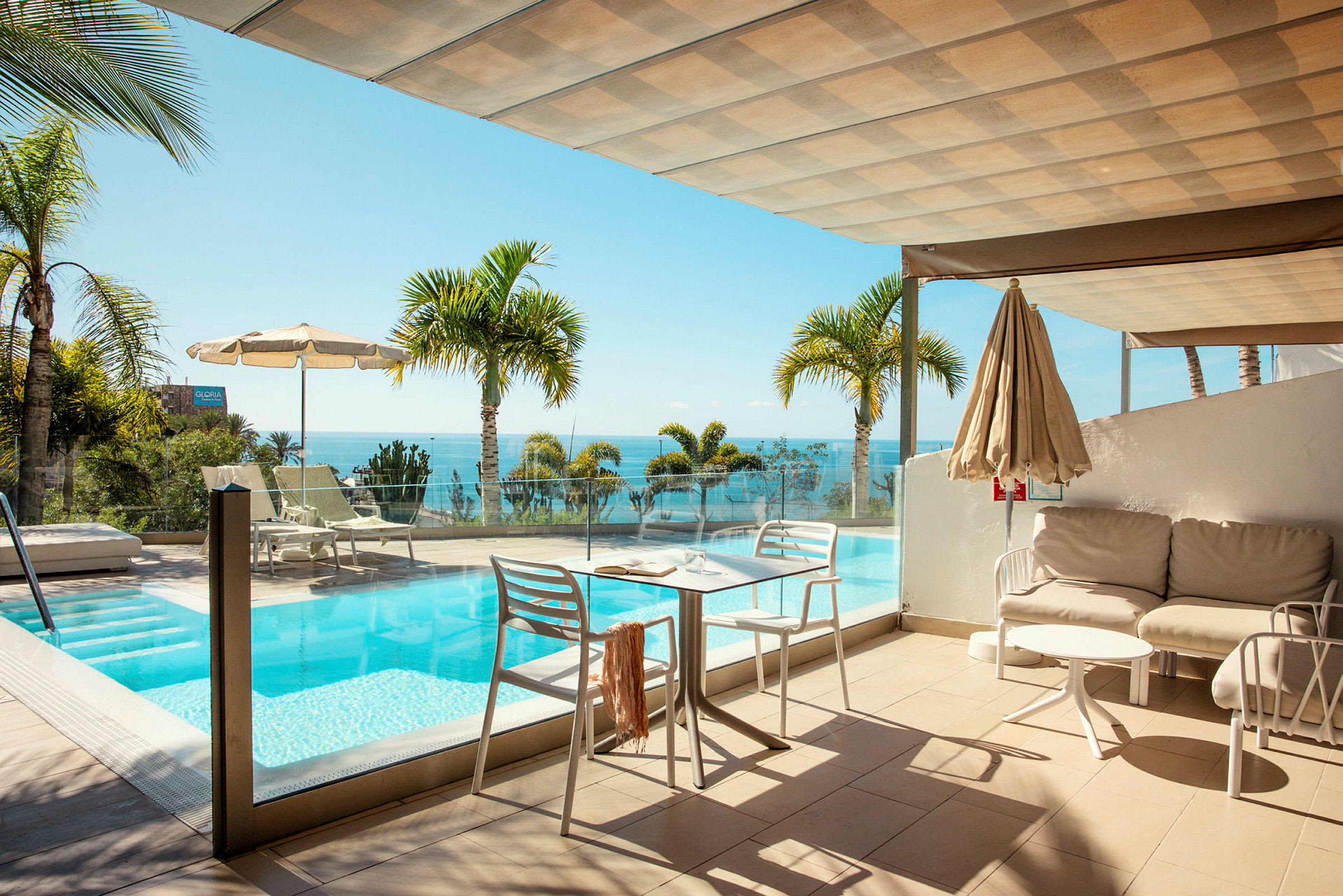 En terrasse med en pool og udsigt over havet, omgivet af palmer. (AI-genereret tekst)