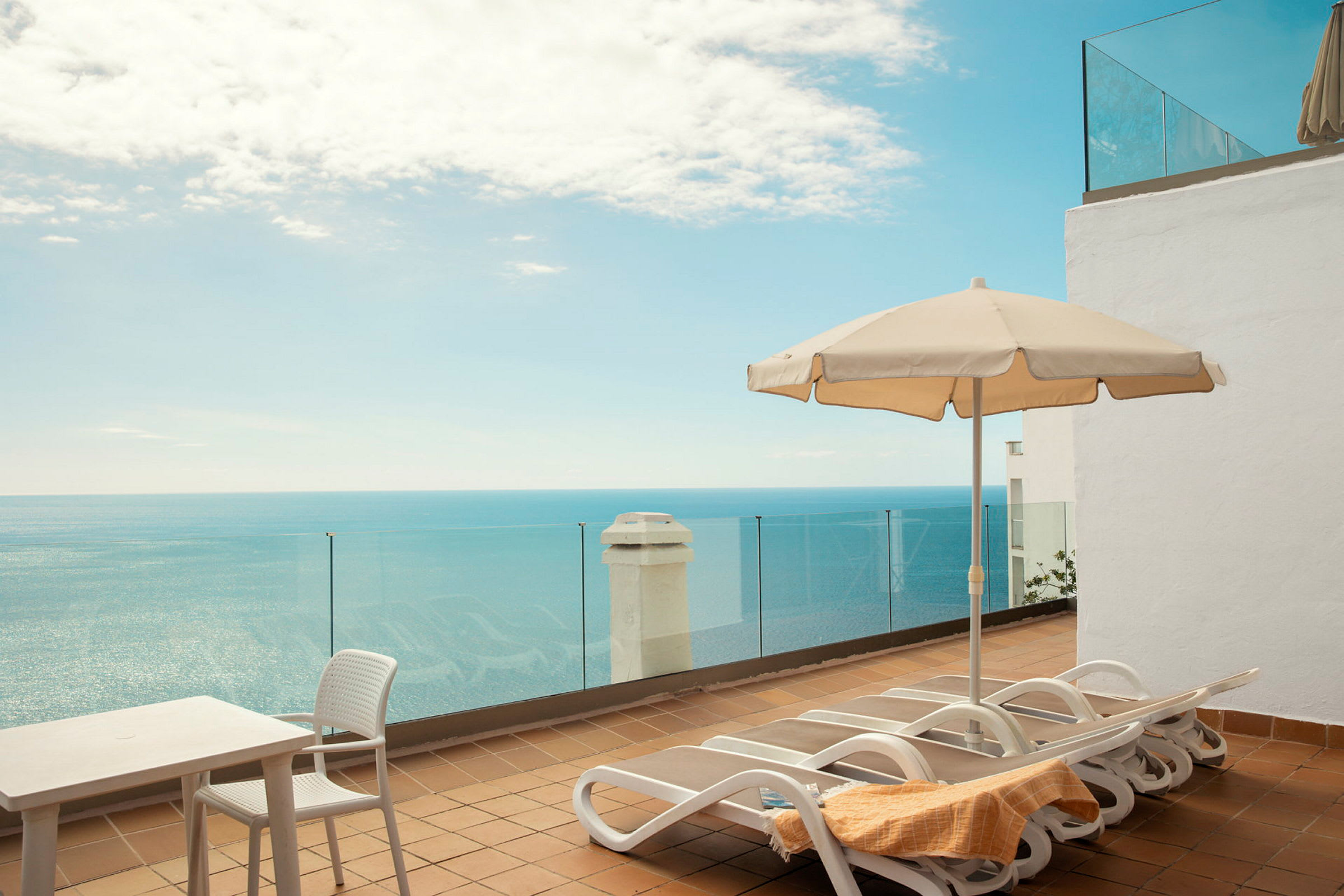 Solterrasse med liggestole, parasol og udsigt over havet. (AI-genereret tekst)