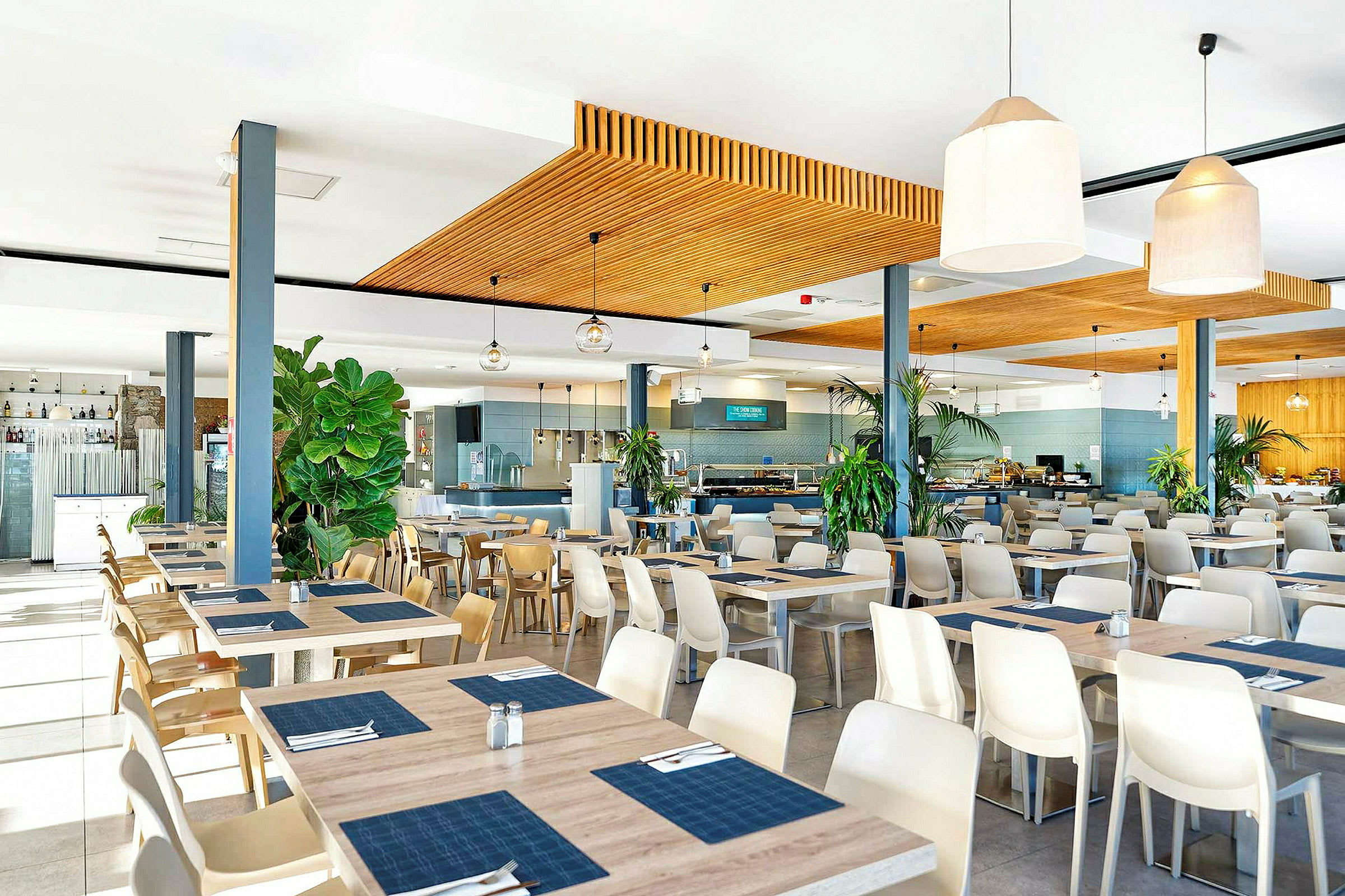 En restaurant med moderne møbler samt borde og stole. Dekorationer inkluderer store potteplanter. (AI-genereret tekst)
