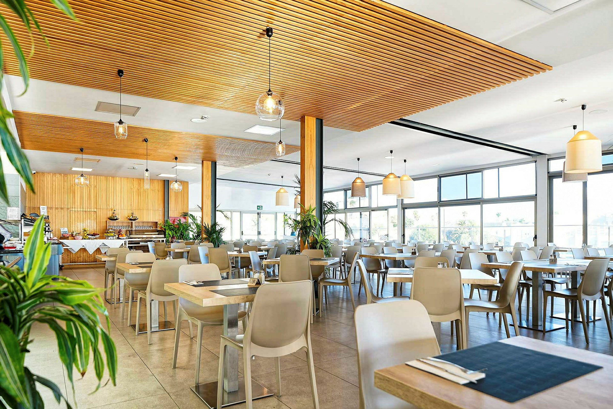 Billede af en lys restaurant med trælister og store vinduer. (AI-genereret tekst)