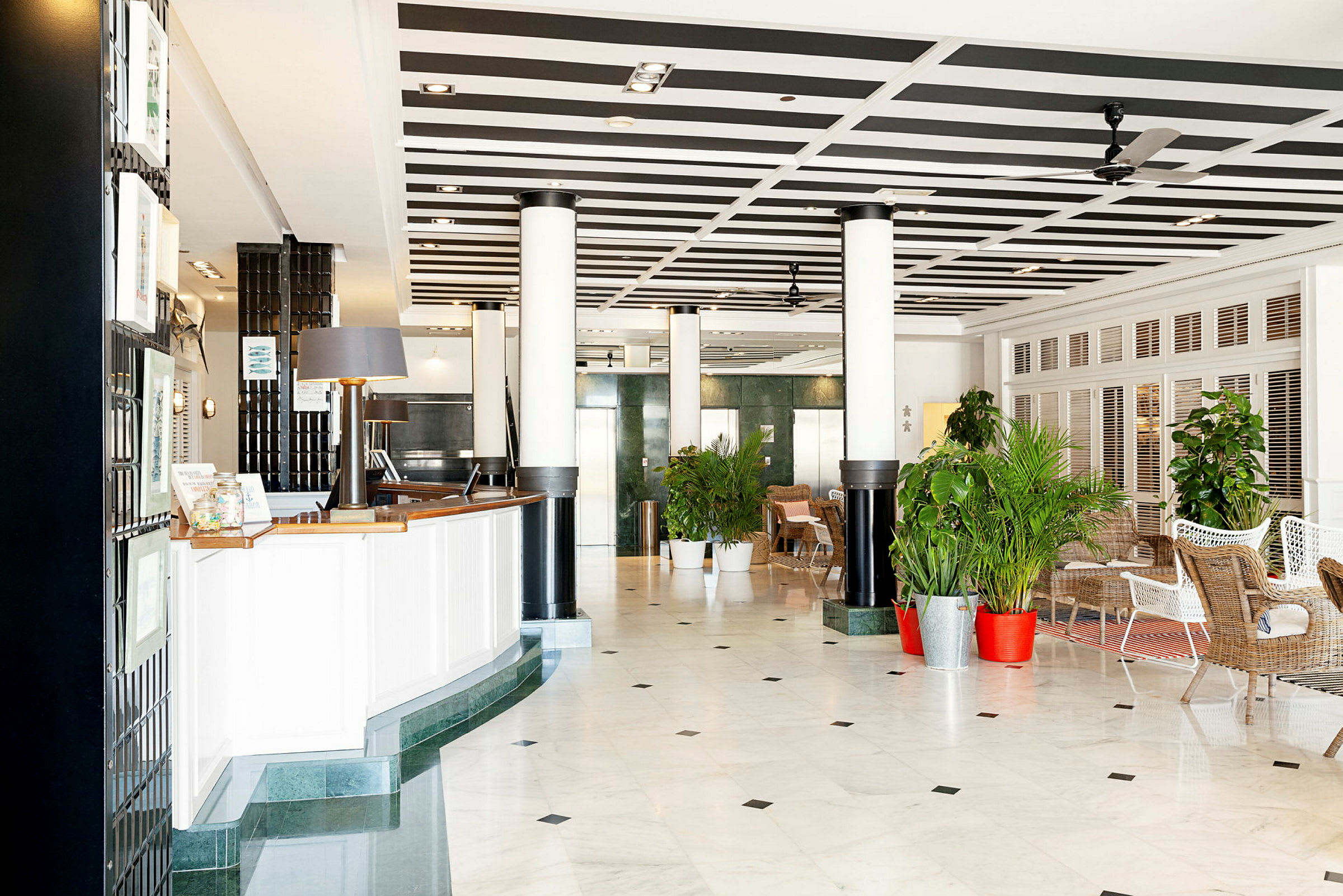 Hotellets lobby med reception og siddegrupper, omgivet af planter. (AI-genereret tekst)