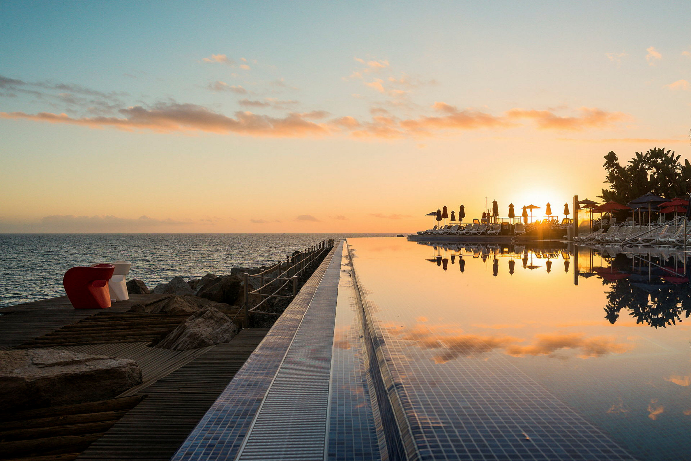 Solnedgang over havet og en infinitypool med liggestole. (AI-genereret tekst)