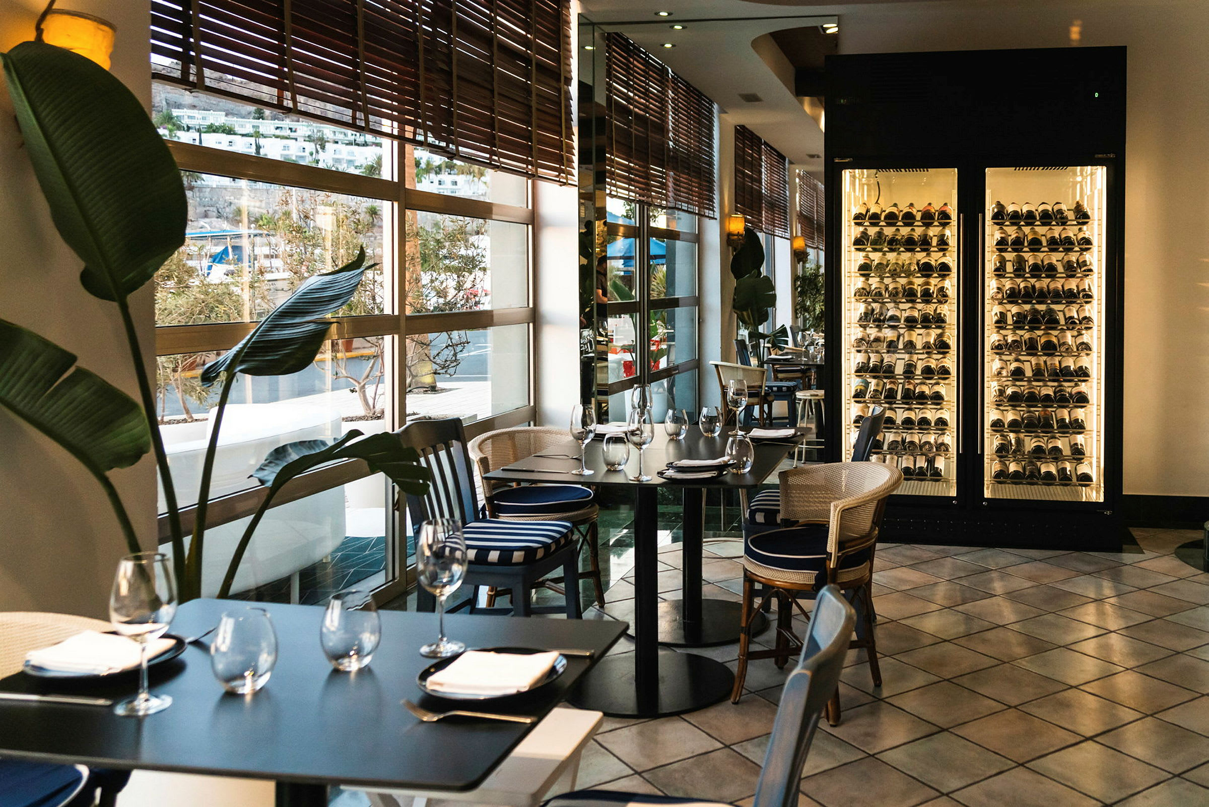Interiør af restaurant med dækkede borde, store vinduer mod udsigt og oplyst vinopbevaring. (AI-genereret tekst)