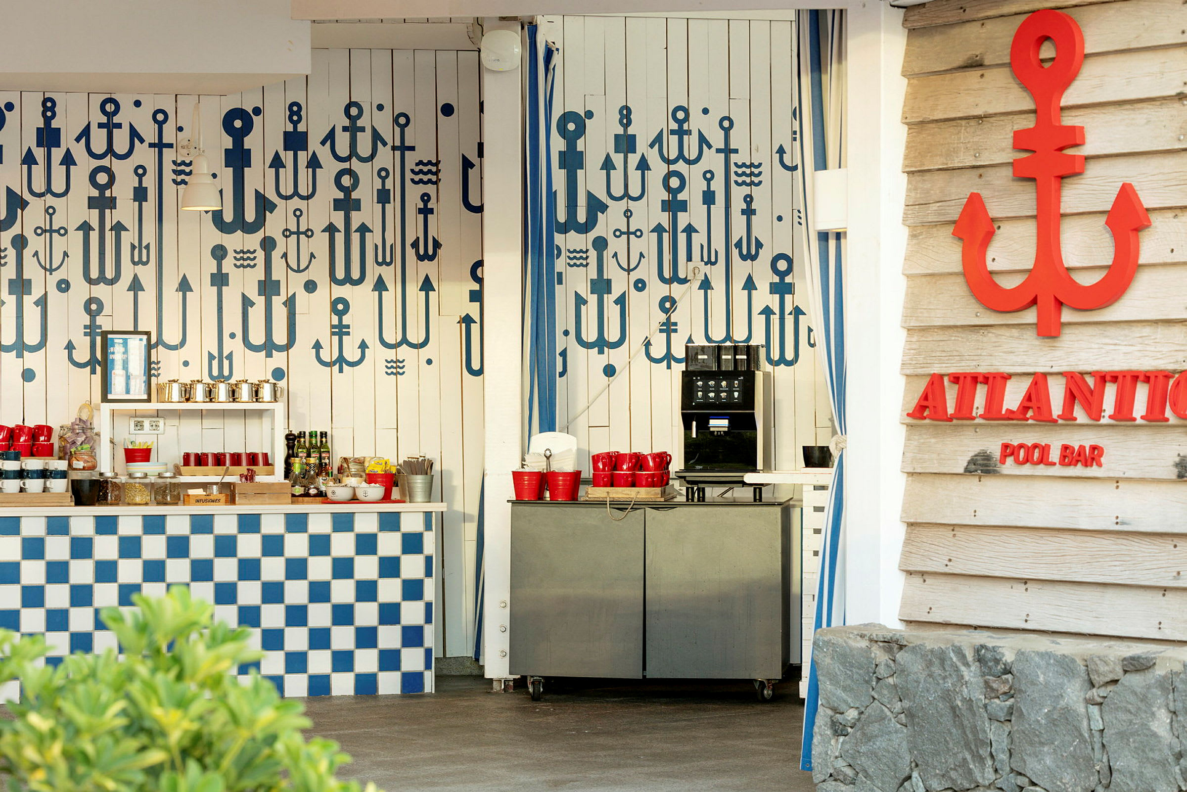 En poolbar med en væg dekoreret med forskellige blå anker motiver, en serveringsdisk med blåt og hvidt ternemønster og en automat med røde kopper. (AI-genereret tekst)