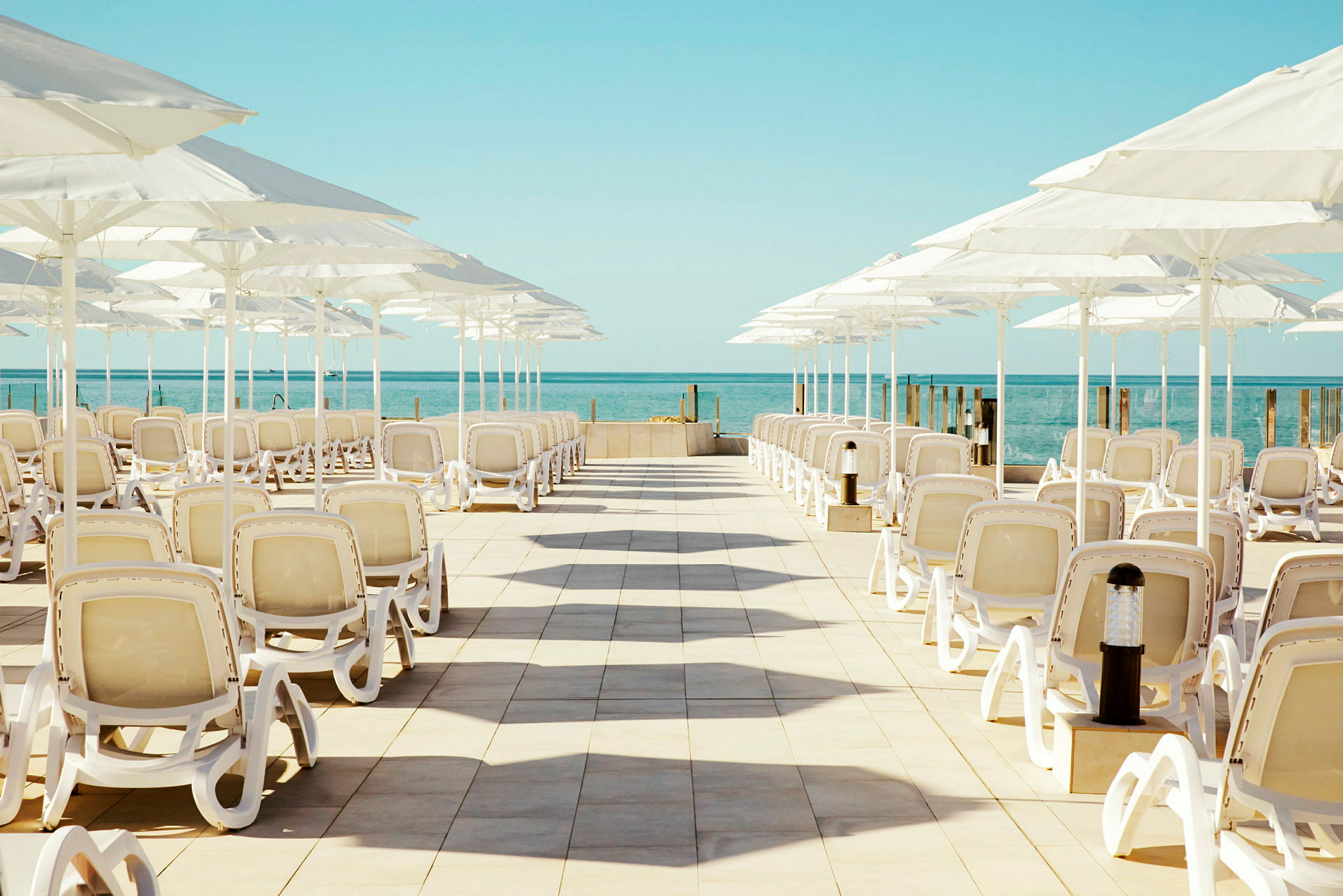Solstole og parasoller opstillet på en terrasse ved havet. (AI-genereret tekst)