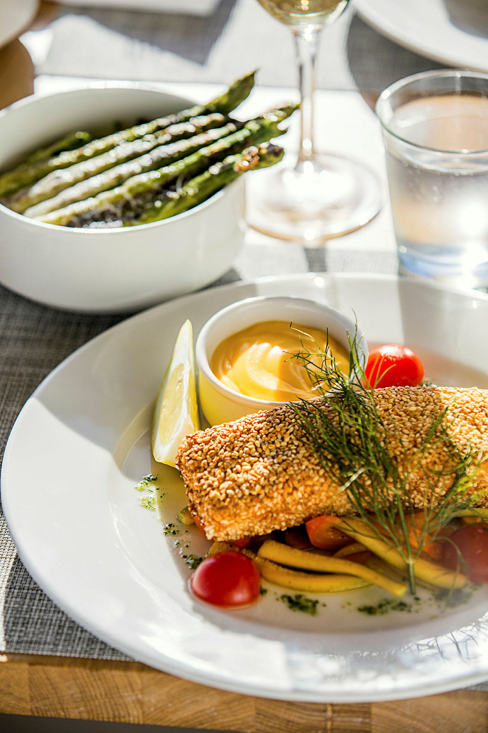 En tallerken med sesampaneret fisk, grøntsager og en skål med sovs, samt en skål med grillet asparges ved siden af. (AI-genereret tekst)