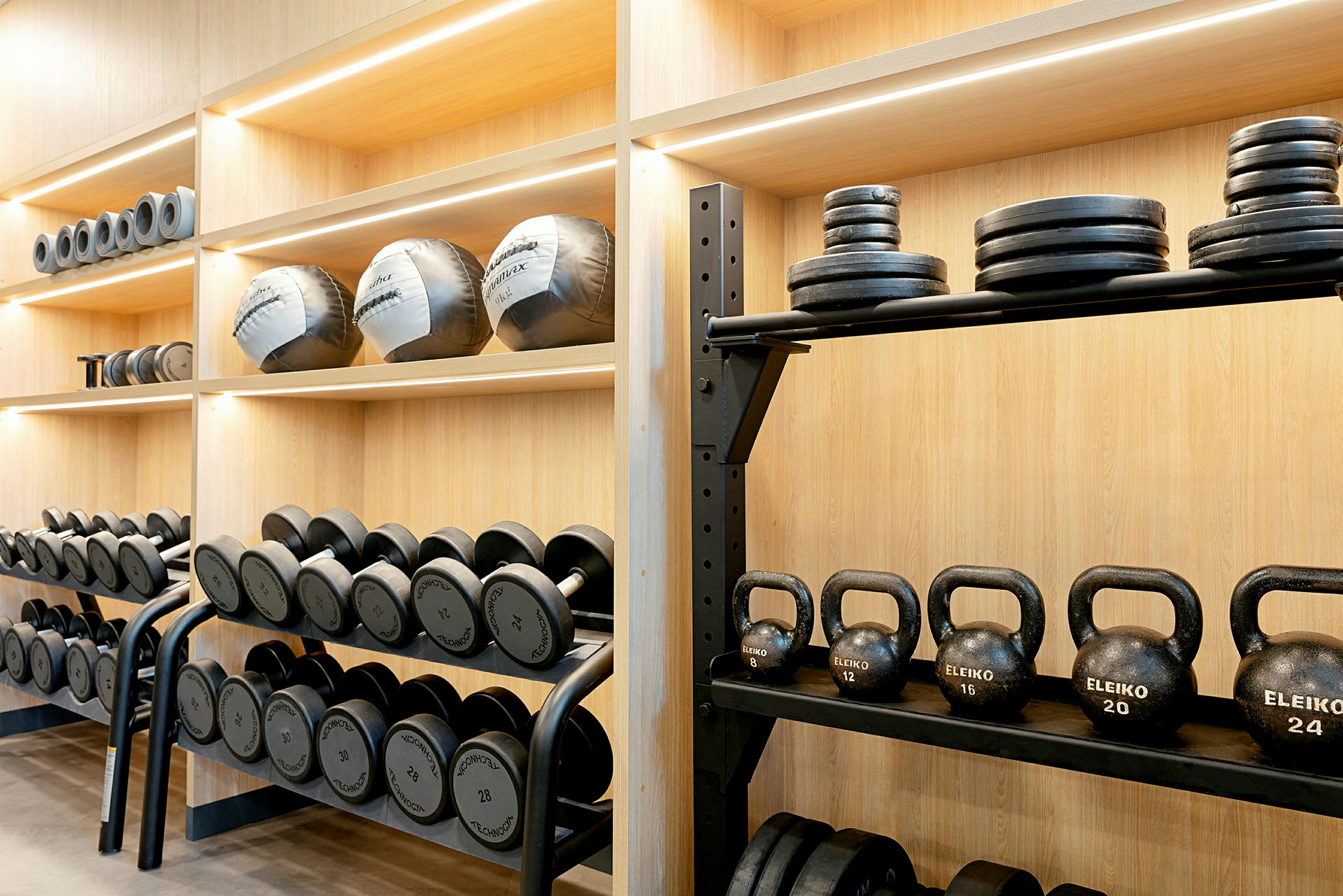 Hylde med forskellige træningsredskaber såsom håndvægte, kettlebells og vægtskiver. (AI-genereret tekst)