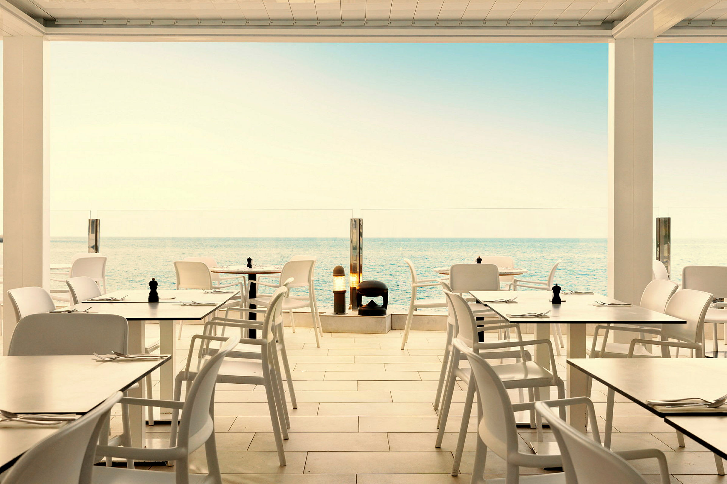 Restaurant med hvide borde og stole med udsigt over havet. (AI-genereret tekst)