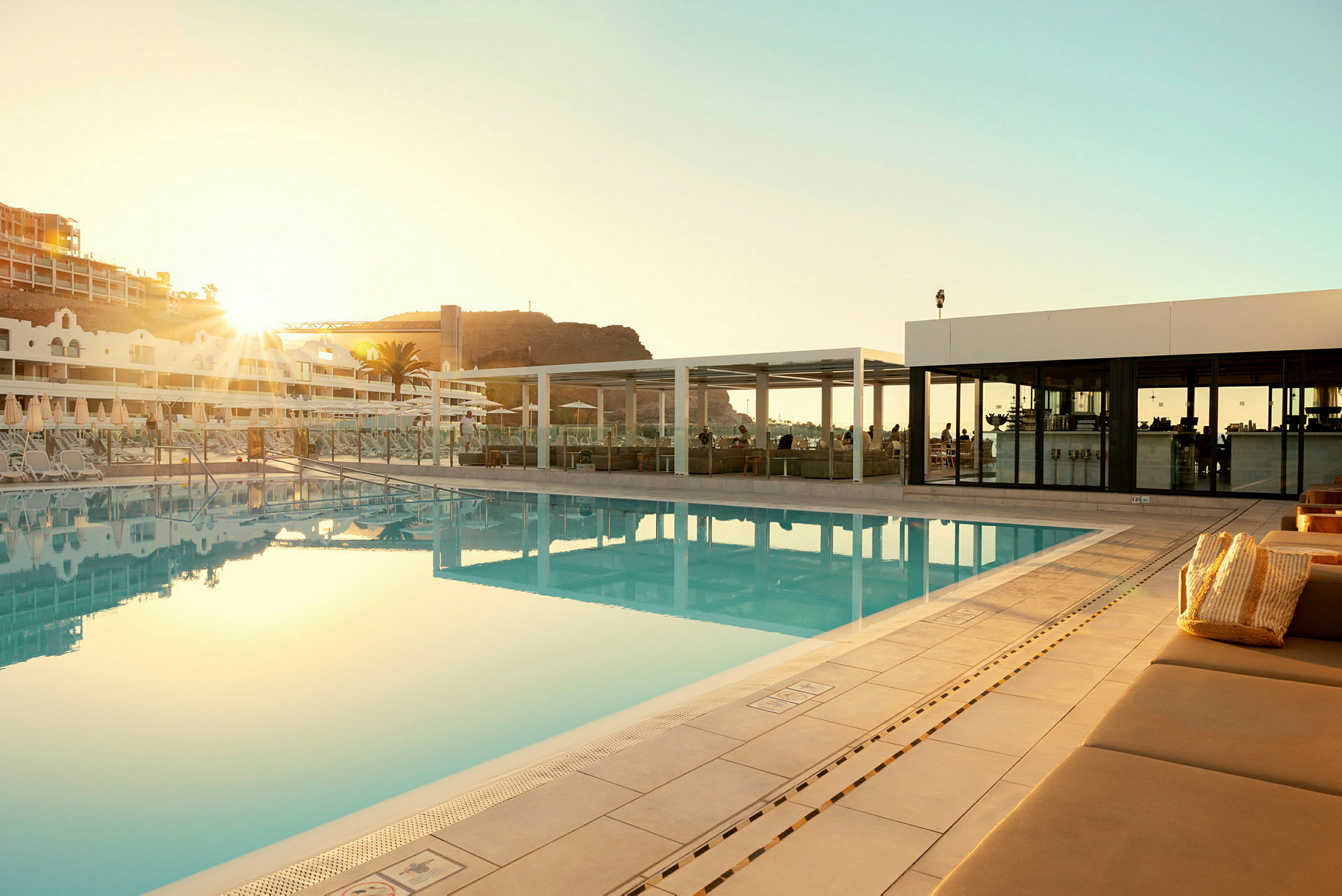 Udendørs swimmingpool ved et hotel med liggestole og en bygning i baggrunden. (AI-genereret tekst)