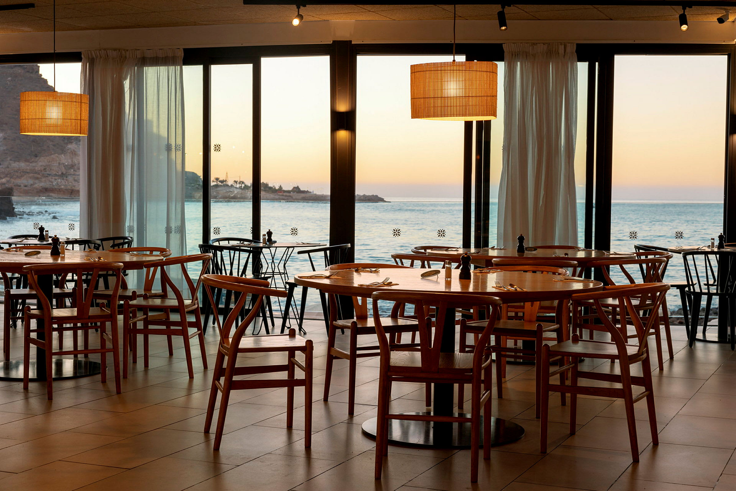 Restaurant med træstole og borde med udsigt over havet og solnedgang. (AI-genereret tekst)
