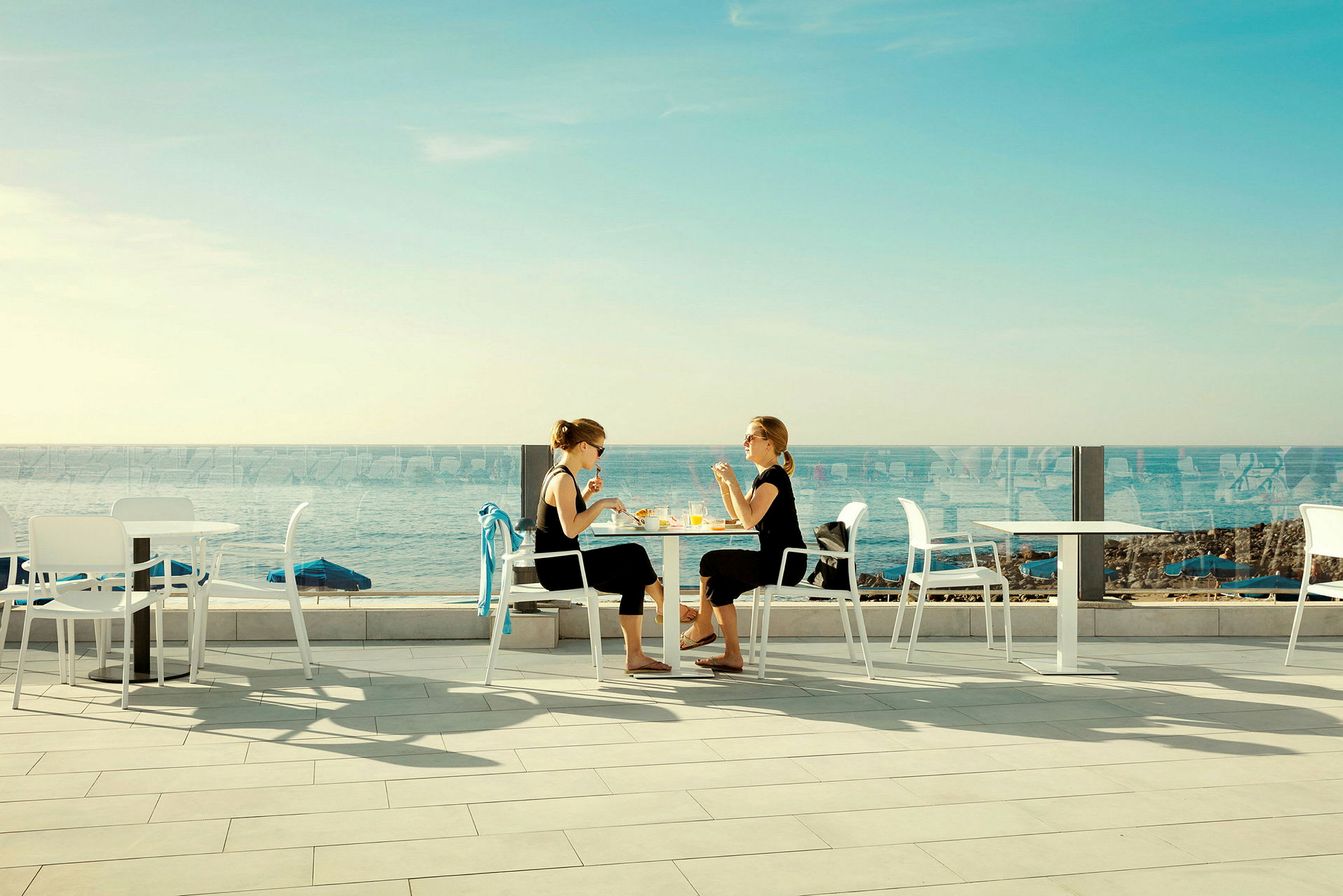 To personer sidder ved et bord udendørs tæt på havet. (AI-genereret tekst)