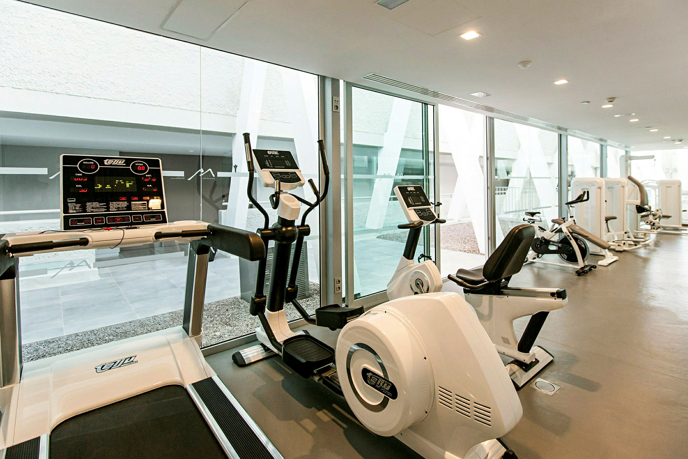 Et fitnesscenter med moderne konditionsmaskiner og store glasvinduer. (AI-genereret tekst)