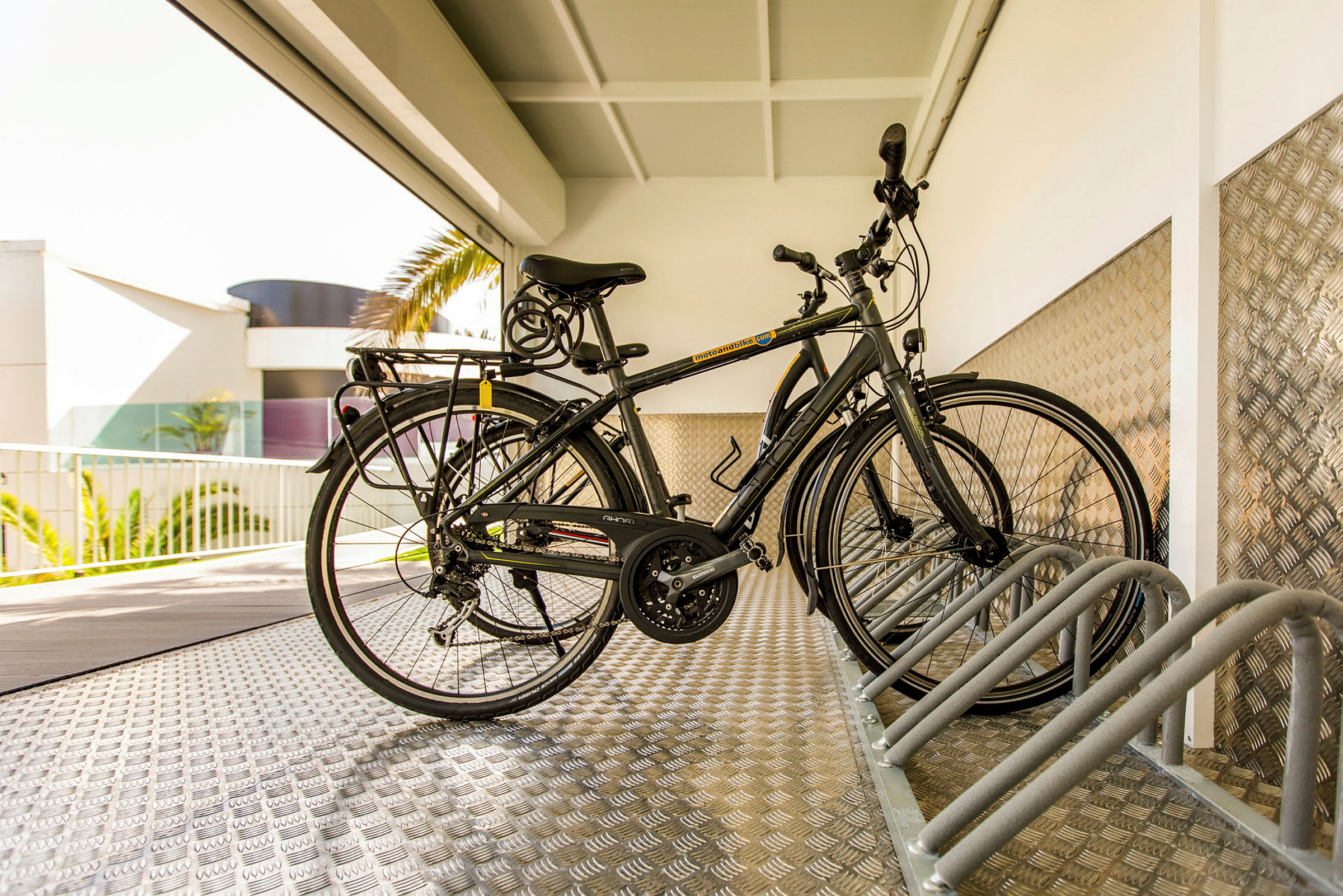 To cykler er parkeret i en cykelstativ under et tag. (AI-genereret tekst)