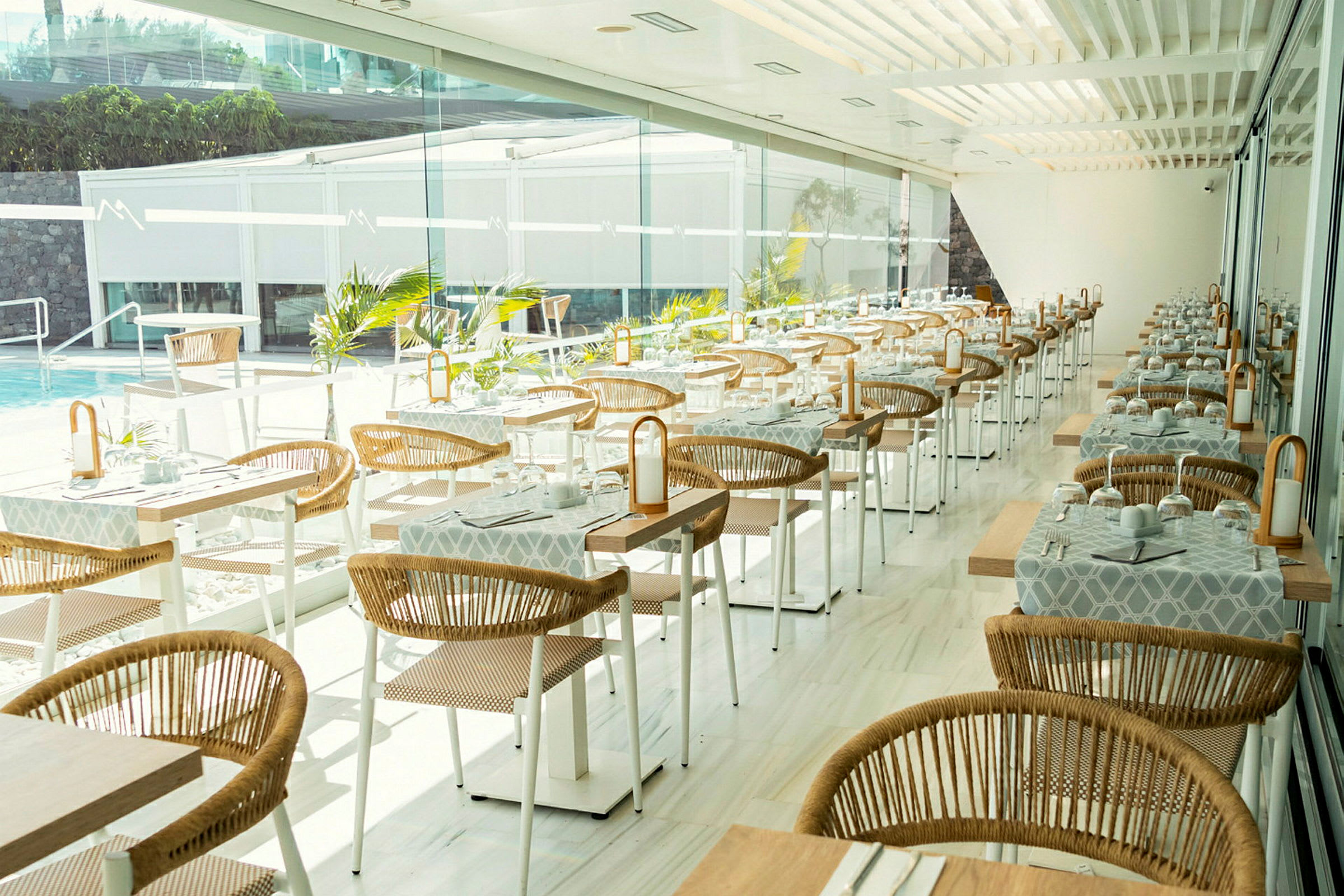 Moderne restaurant med opdækkede borde og rottingstole ved store vinduer. (AI-genereret tekst)