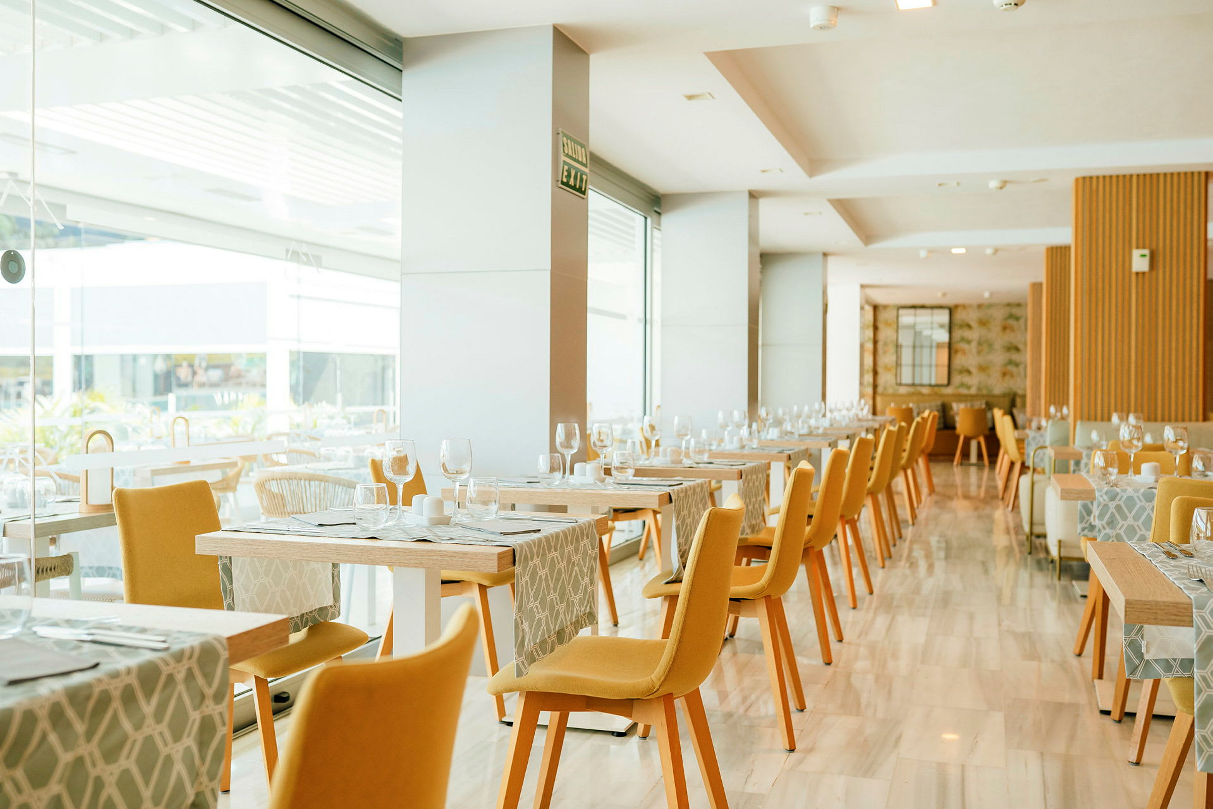 Billede af en lys restaurant med gule stole og opdækkede borde. (AI-genereret tekst)