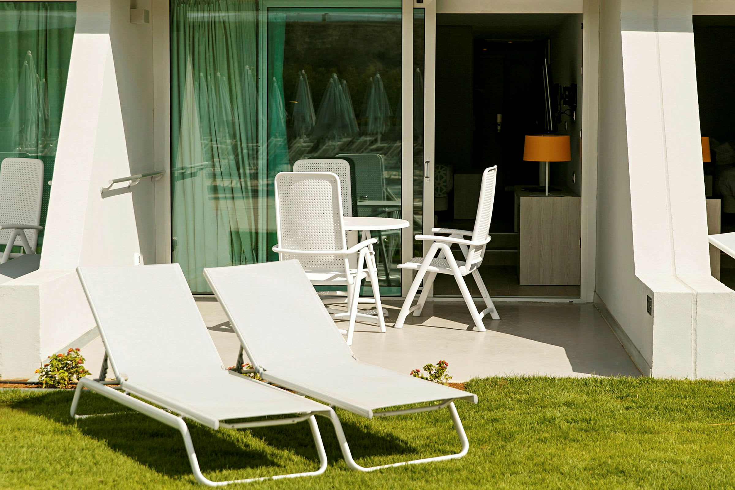 To liggestole på græsplænen foran en terrasse med bord og stole. (AI-genereret tekst)