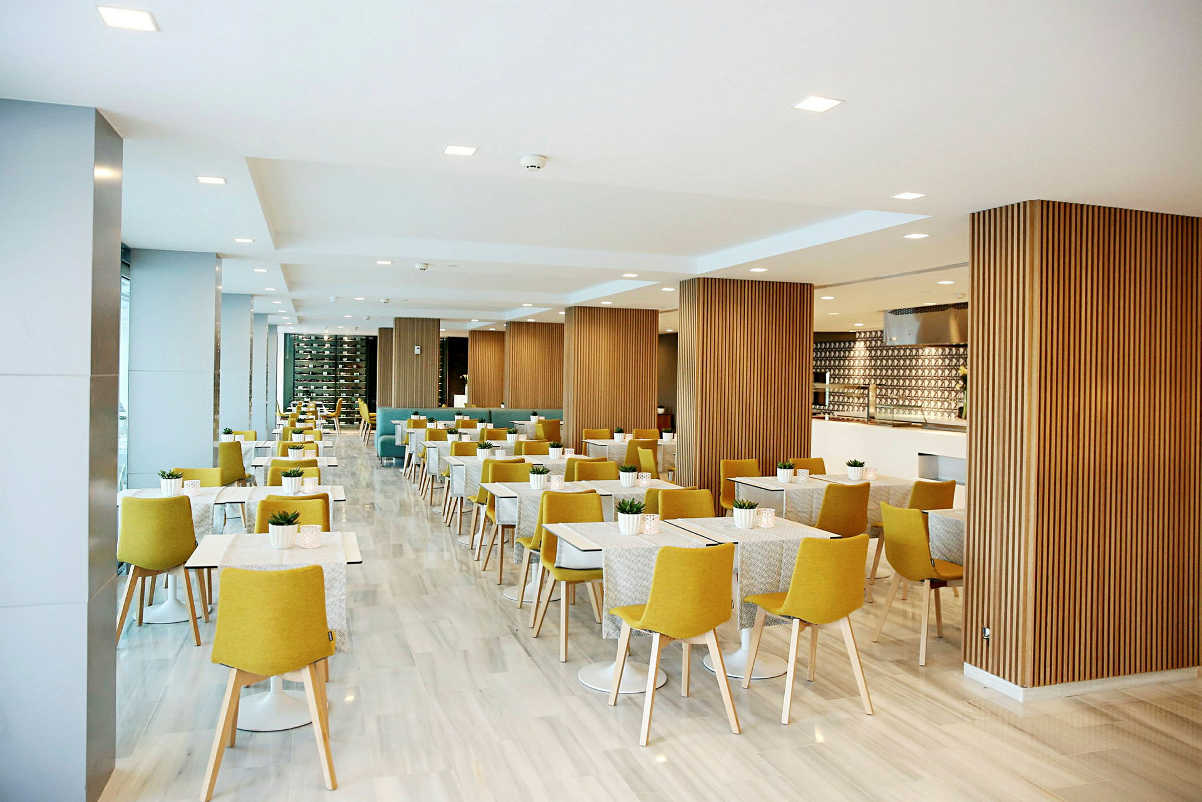 Restaurant med lys indretning, gule stole og hvide borde. (AI-genereret tekst)