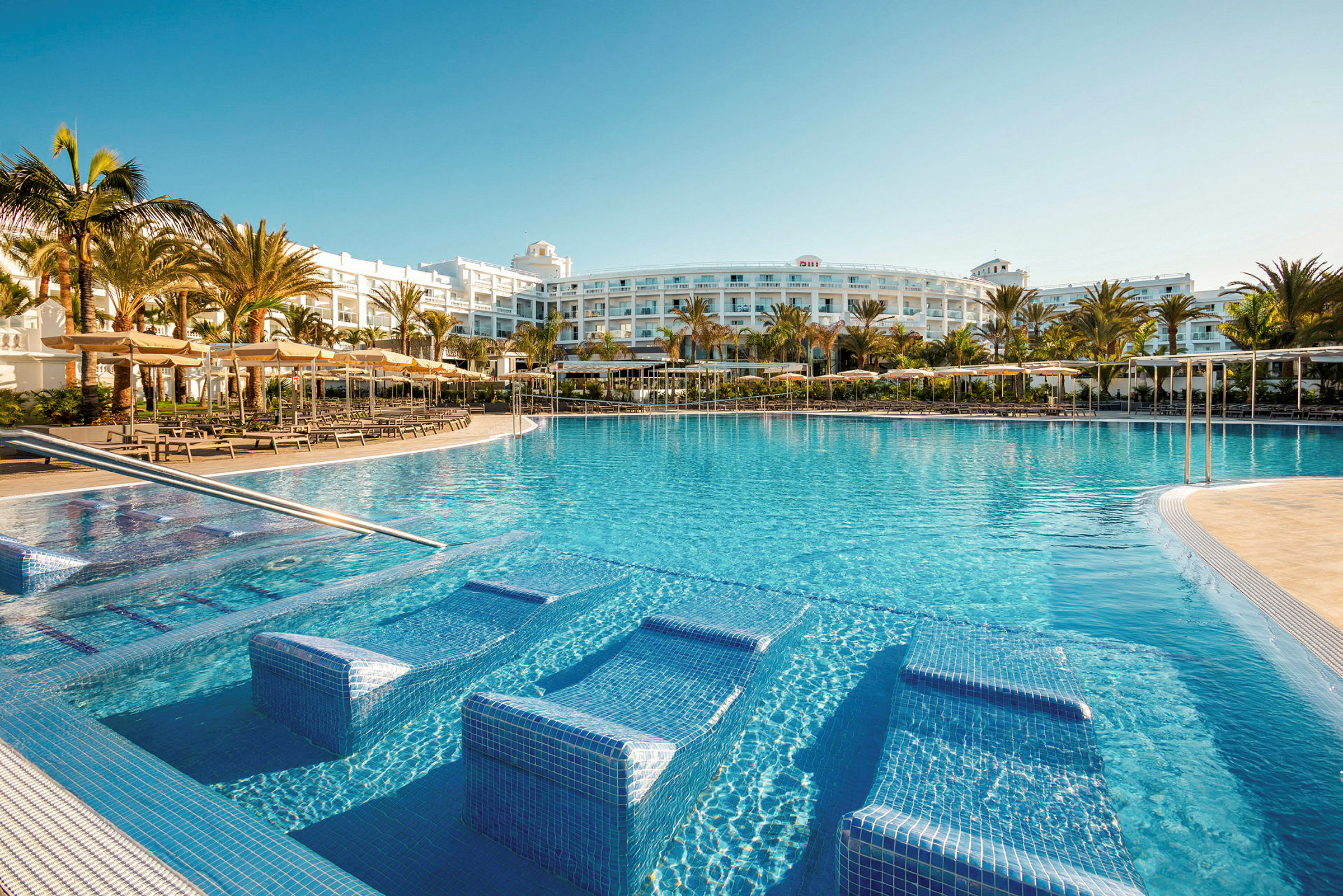 Billede af en stor udendørs pool foran en hotelbygning. (AI-genereret tekst)