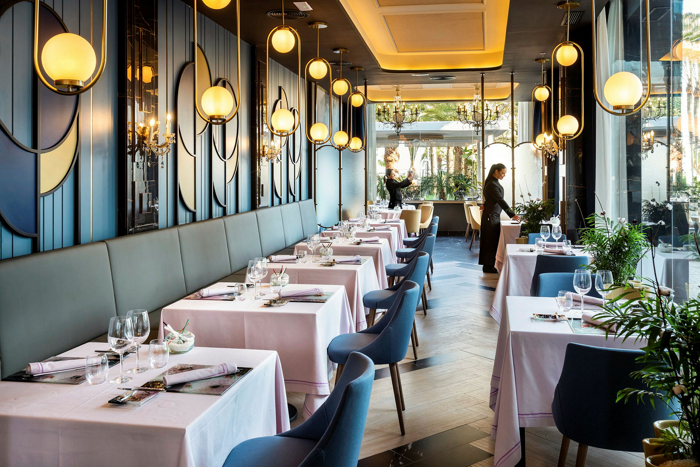 En elegant restaurant med dækkede borde, blå stole og moderne belysning langs væggene. (AI-genereret tekst)