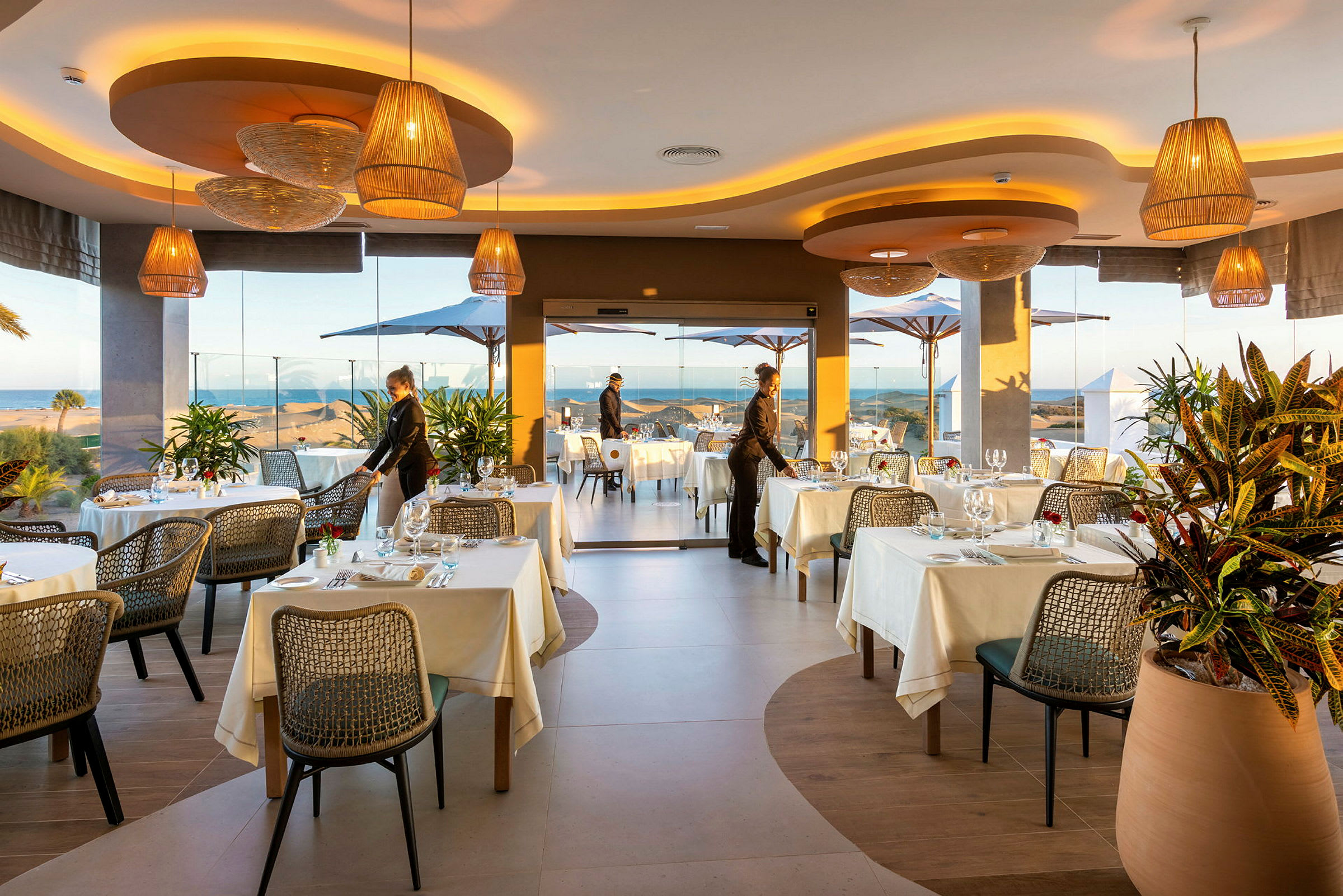 Restaurant med dækkede borde, planteudsmykning og udsigt over havet. (AI-genereret tekst)
