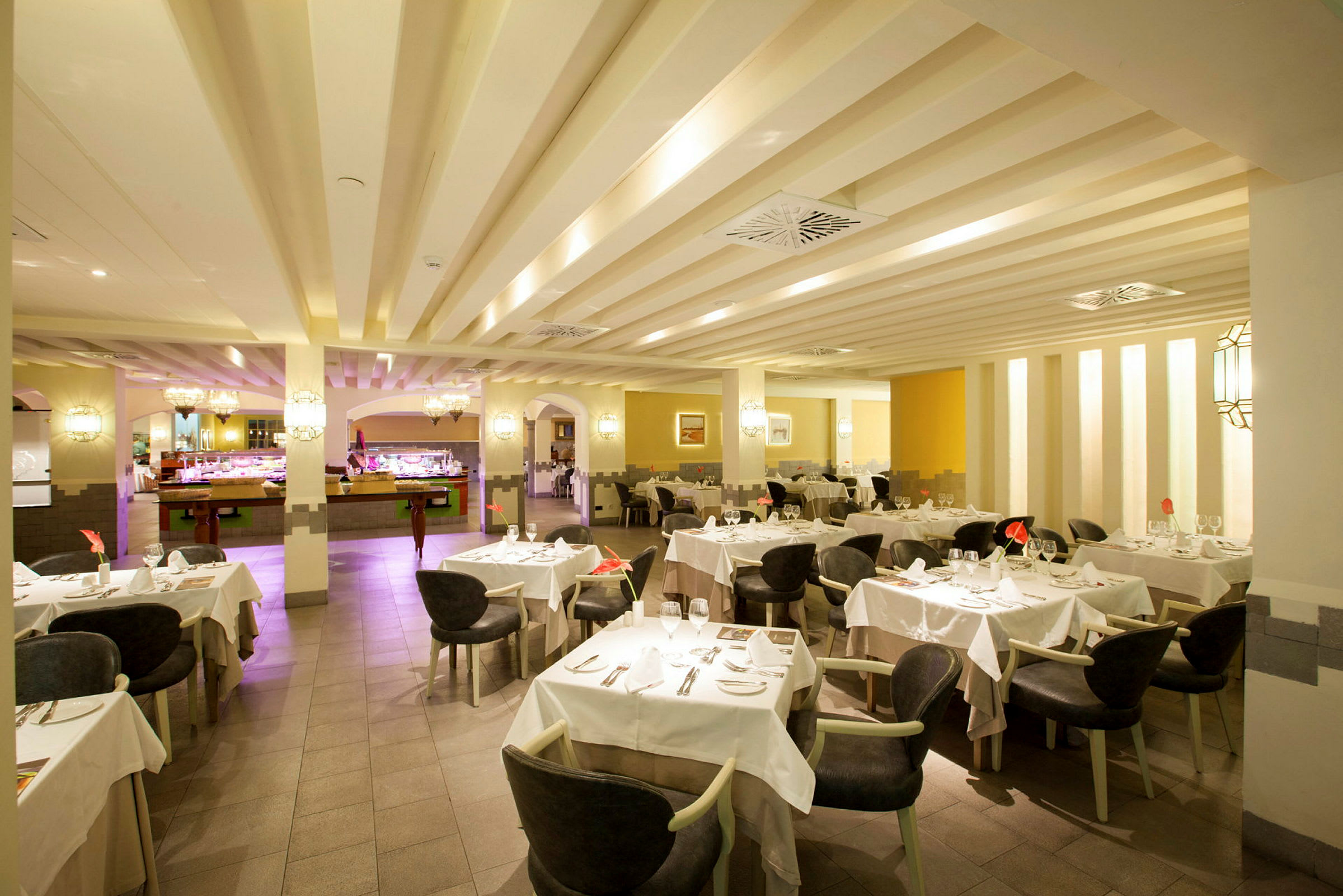 En rummelig restaurant med dækkede borde og stole, oplyst interiør med buffetdisk i baggrunden. (AI-genereret tekst)