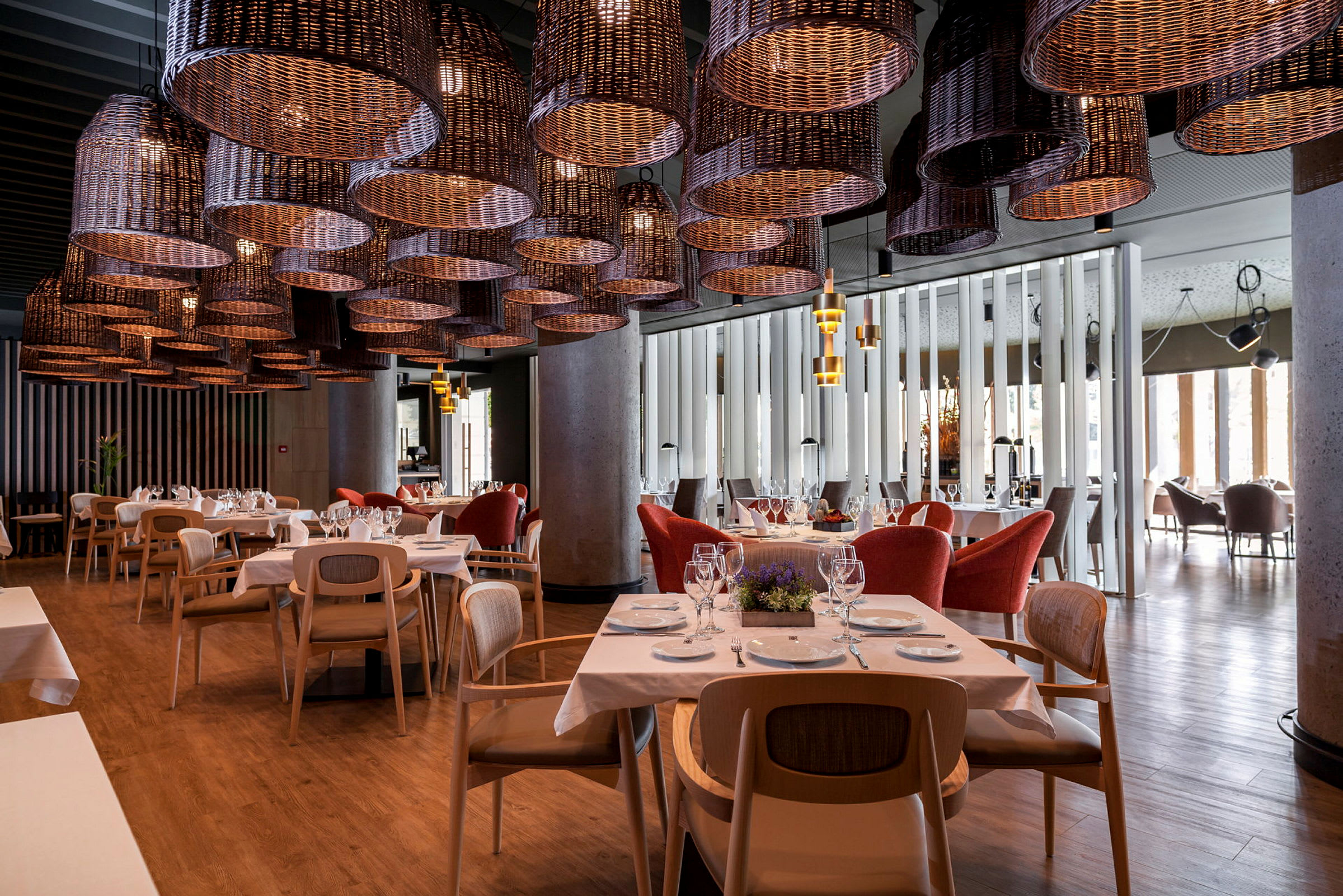 Restaurant med dækkede borde, moderne træstole og store kurvelamper i loftet. (AI-genereret tekst)