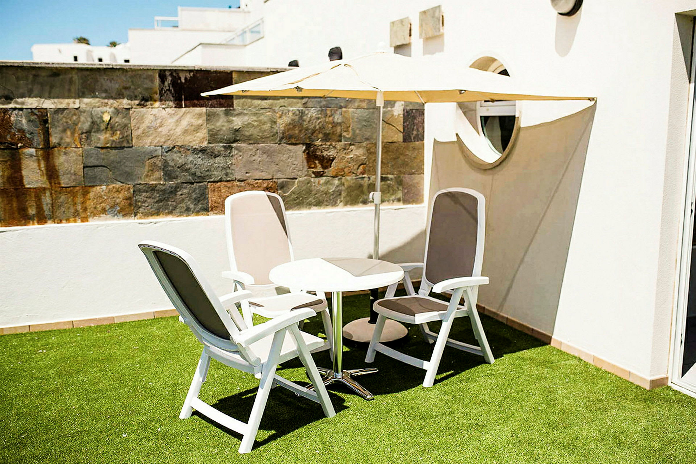 Billede af en terrasse med græs, fire stole og et bord under en parasol. (AI-genereret tekst)