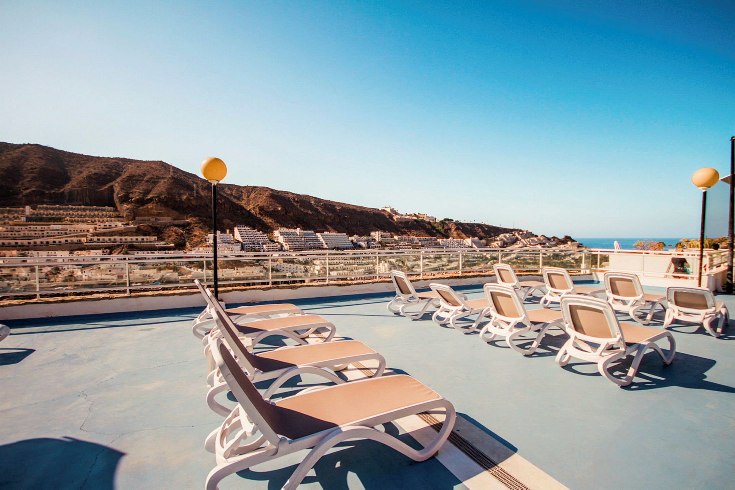Liggestole på en terrasse med udsigt over bjergene og havet. (AI-genereret tekst)