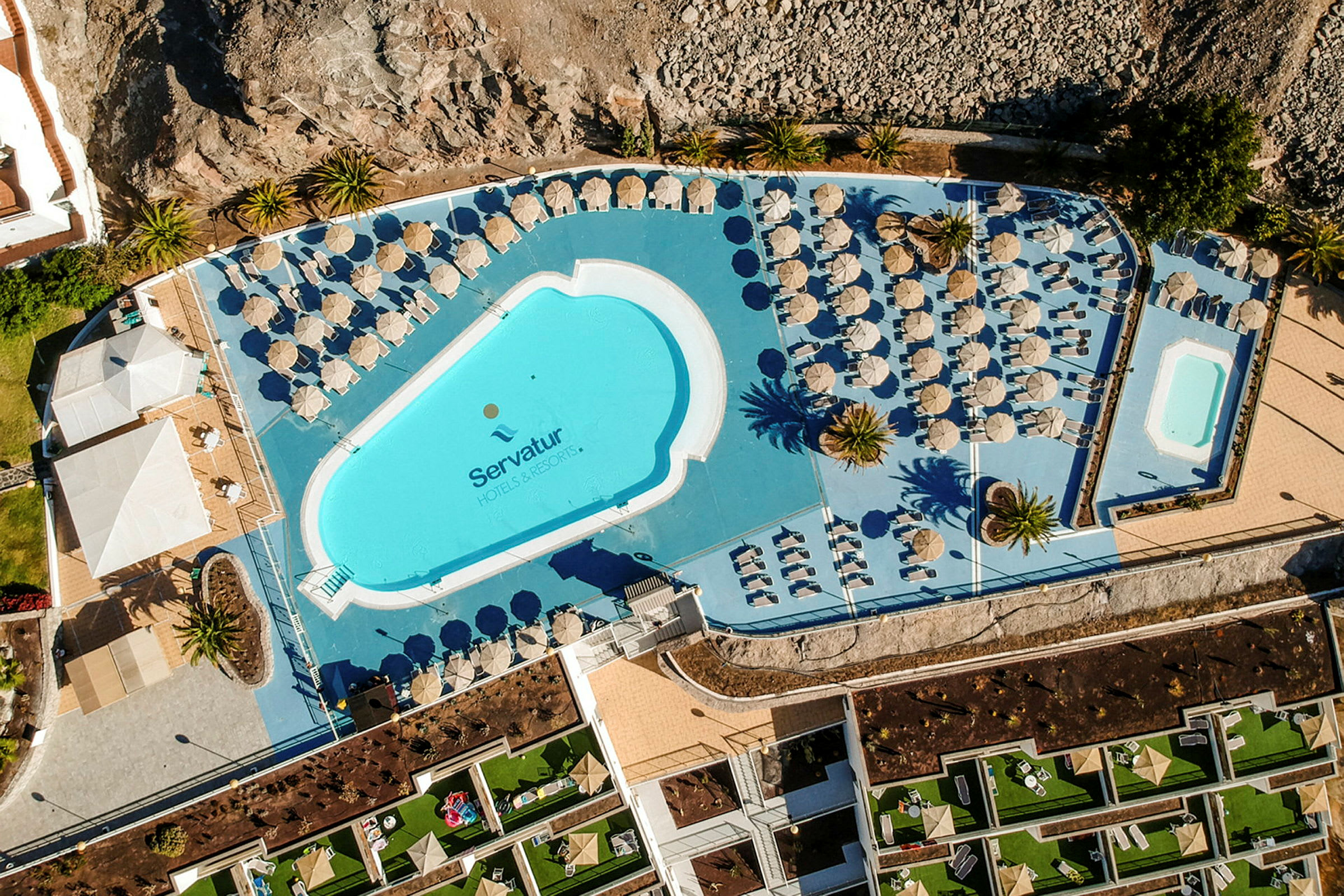Luftfoto af poolområdet på et hotel med solsenge og parasoller. (AI-genereret tekst)