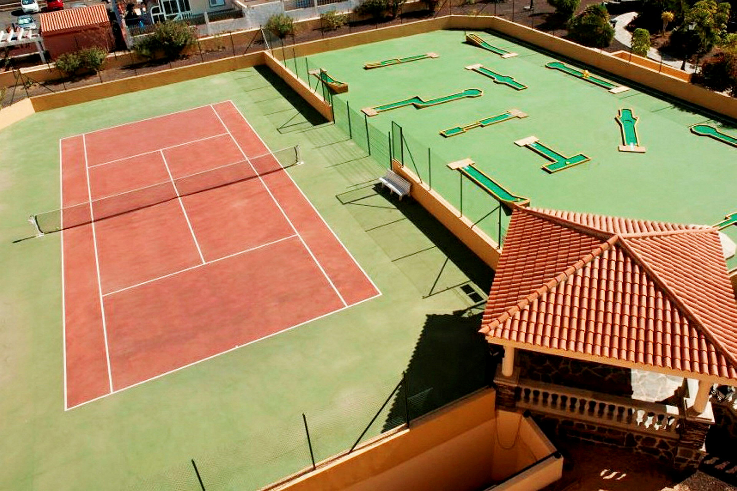 Tennisbane og minigolfområde ved siden af en bygning med rødt tag. (AI-genereret tekst)