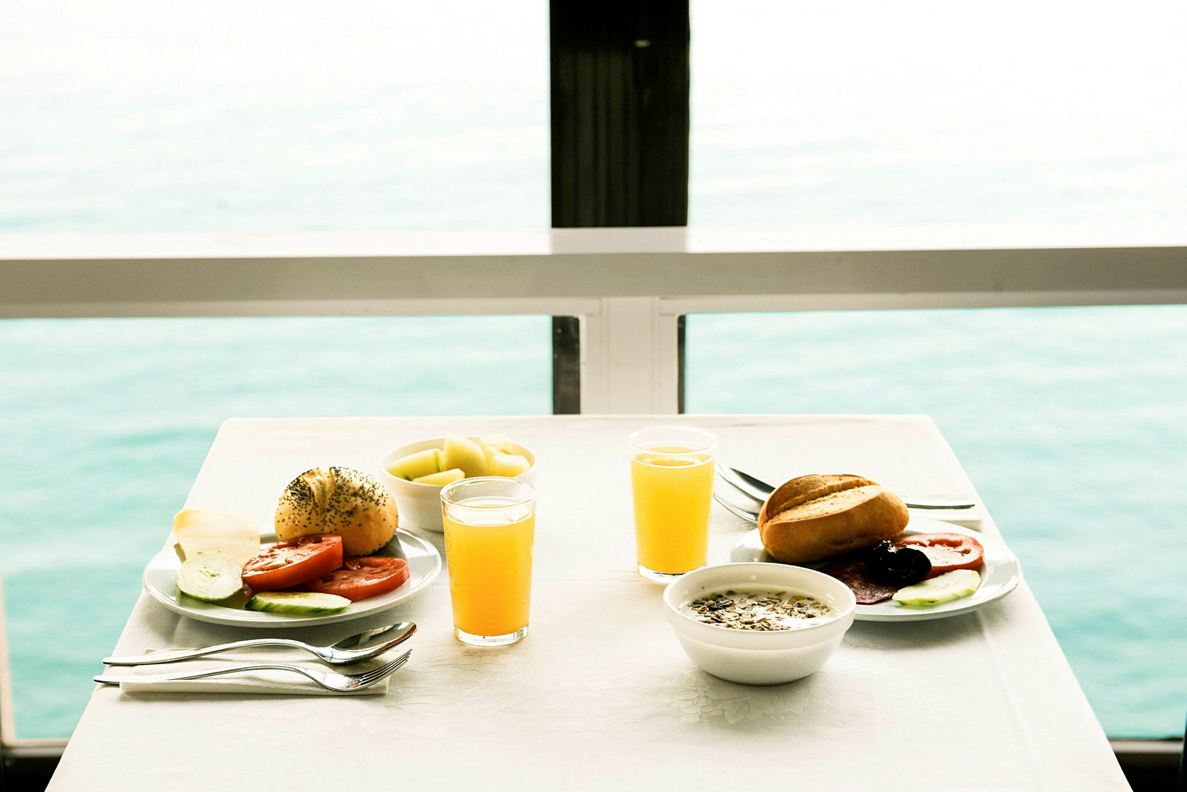 To tallerkener med morgenmad, juiceglas og udsigt over havet. (AI-genereret tekst)