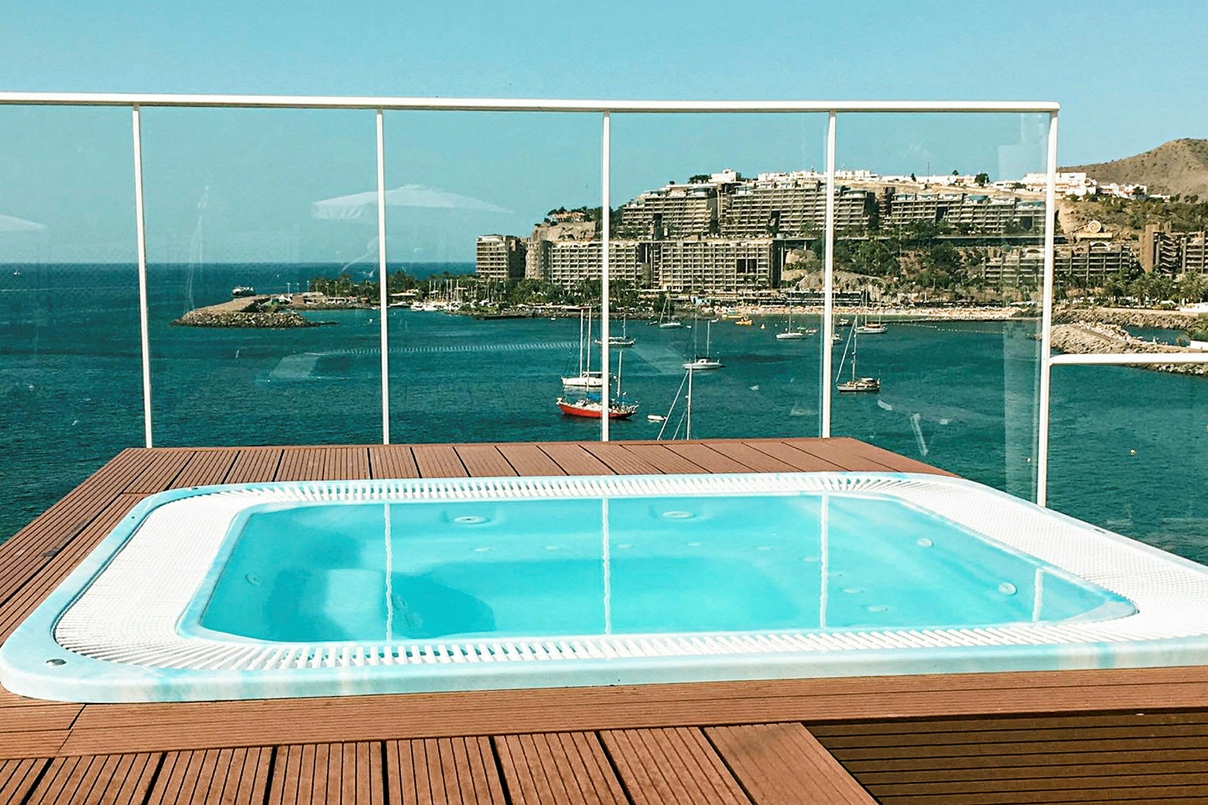 Billede af en jacuzzi med panoramaudsigt over en havn og bygninger ved en kyst. (AI-genereret tekst)