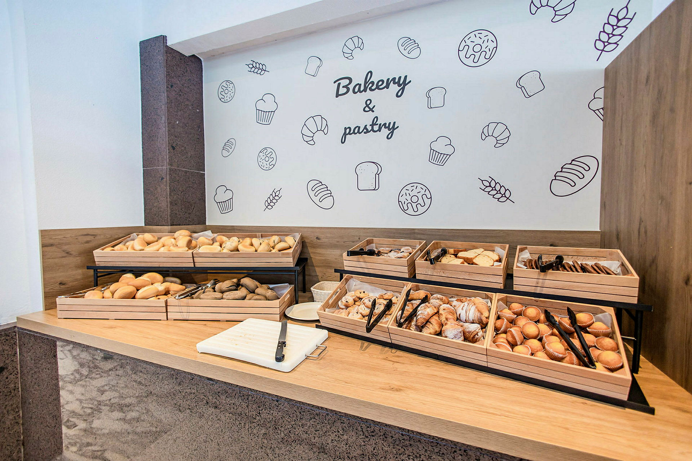 Brød, bagværk og kager er anbragt i trækasser på en buffet. (AI-genereret tekst)