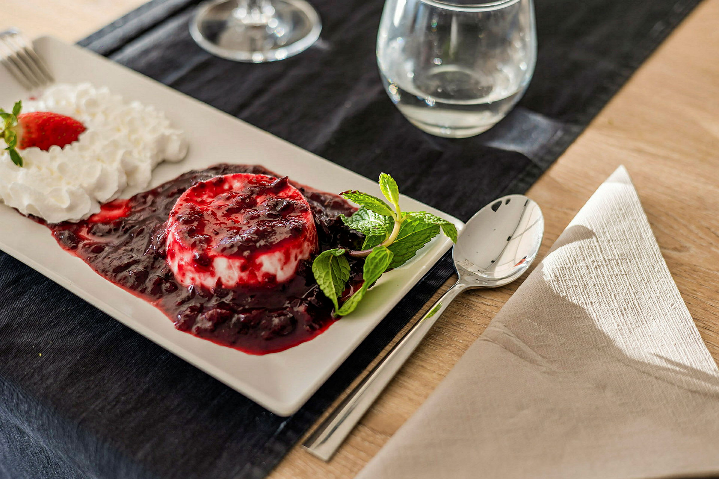 Dessert med fløde, jordbær og bærsauce på en tallerken ved siden af en ske og serviet. (AI-genereret tekst)