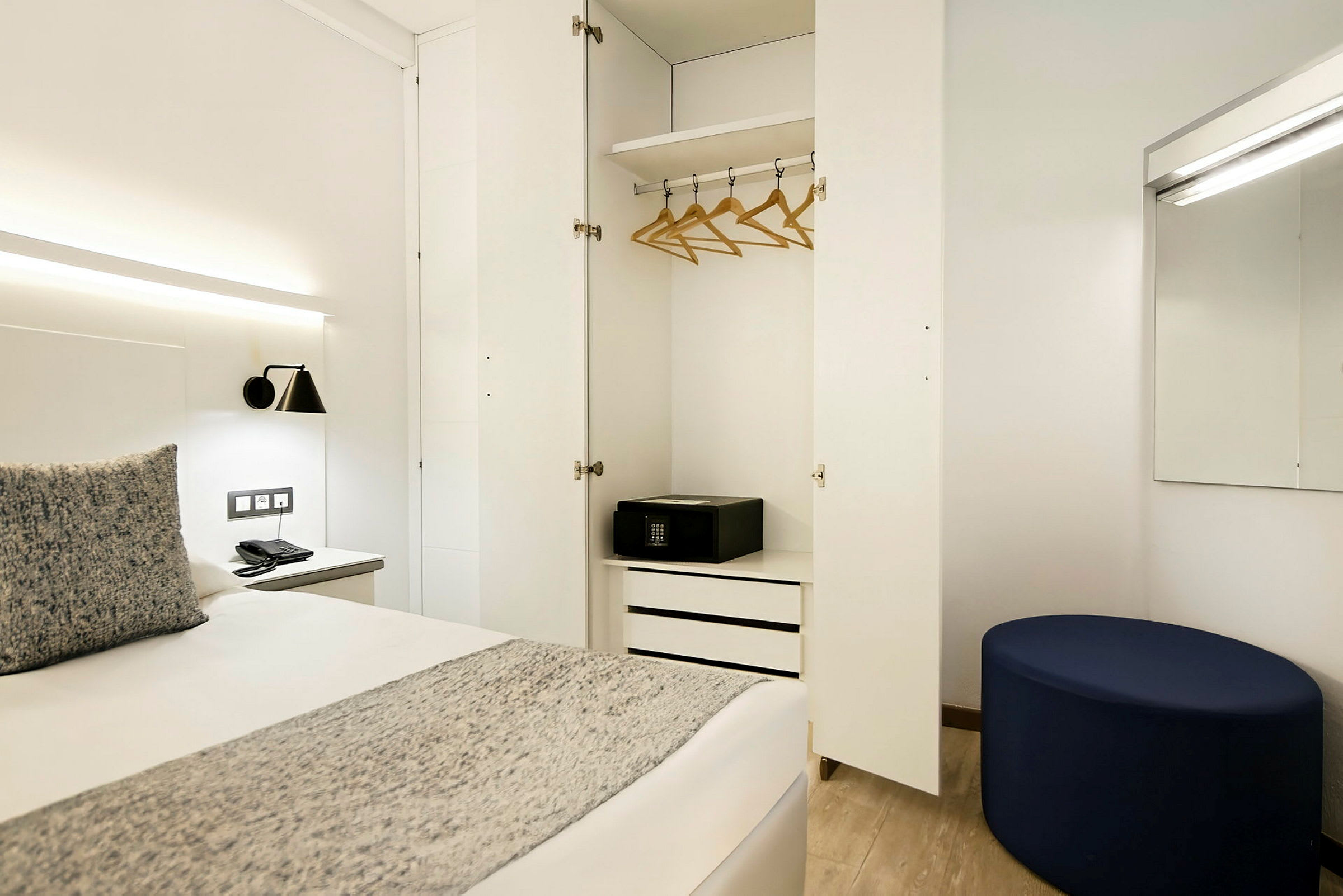 Et hotelværelse med åben garderobe, seng og spejl. (AI-genereret tekst)