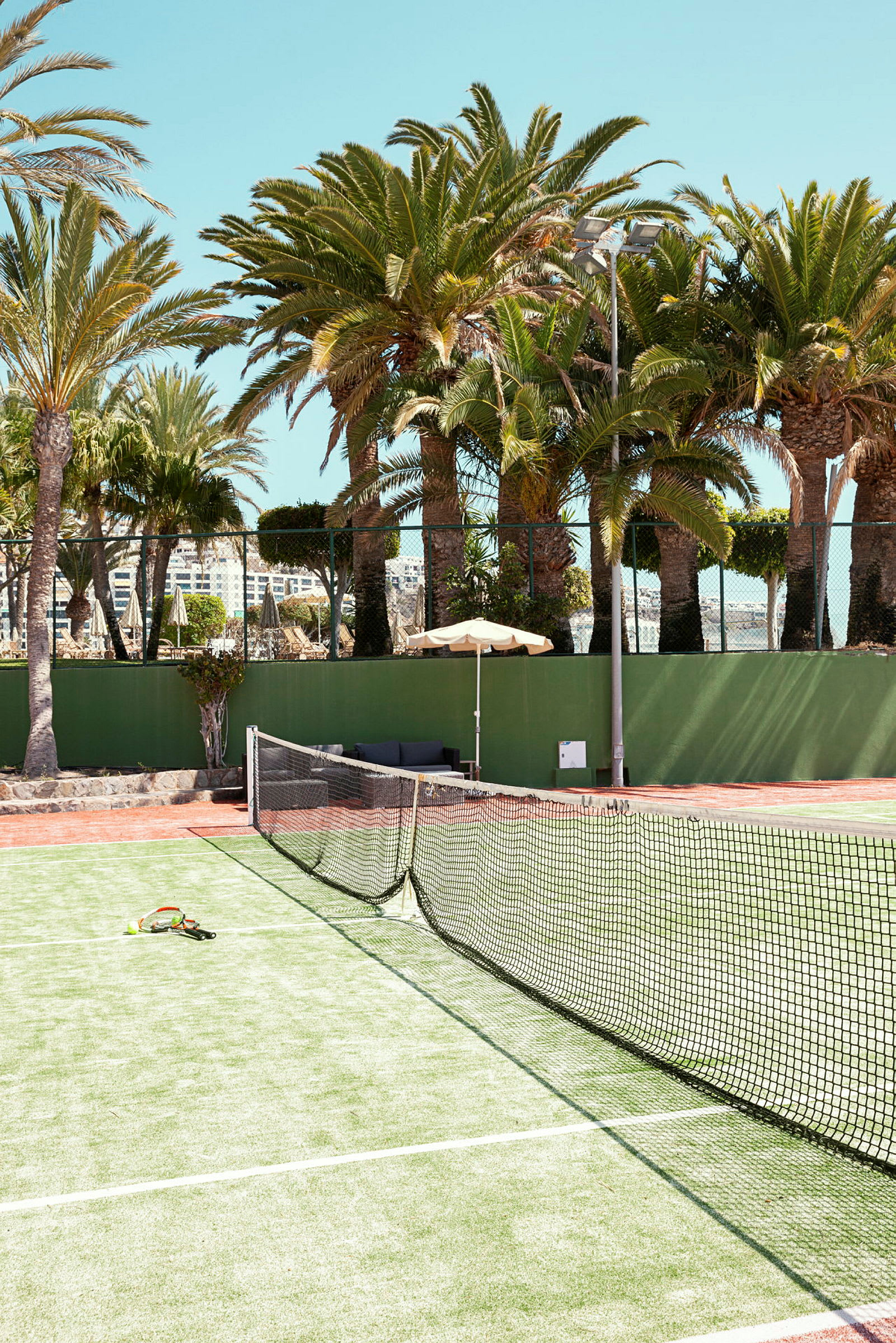 En tennisbane med net og ketsjere, omgivet af palmer. (AI-genereret tekst)
