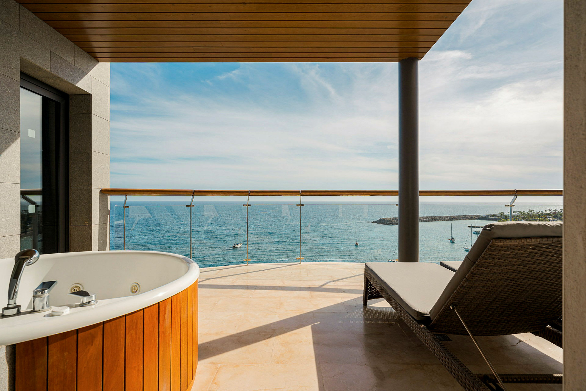 En hotelaltan med jacuzzi og solseng, udsigt over havet og småbåde. (AI-genereret tekst)