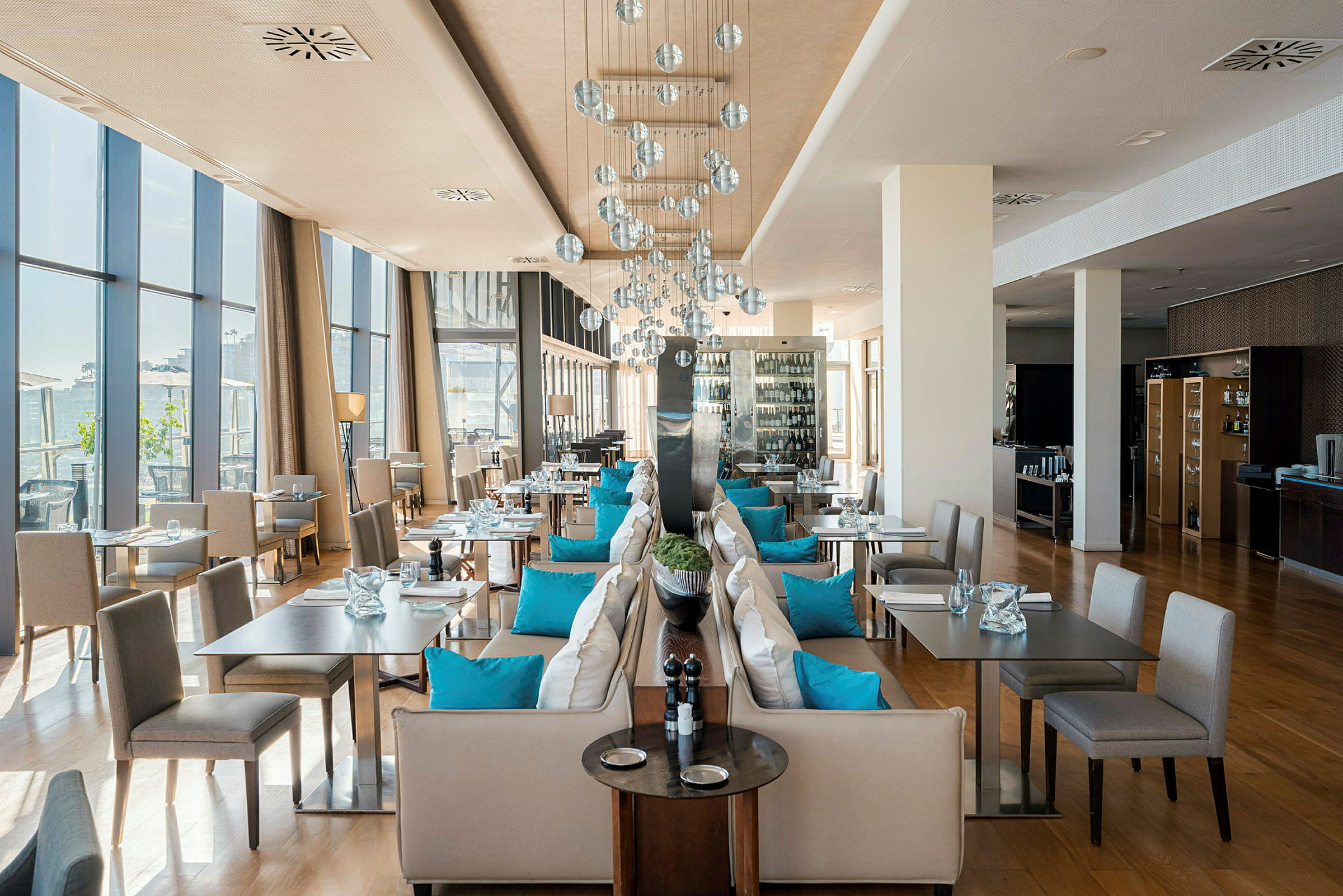 En stilfuld restaurant med store vinduer, bænke dekoreret med blå puder og moderne lamper. (AI-genereret tekst)