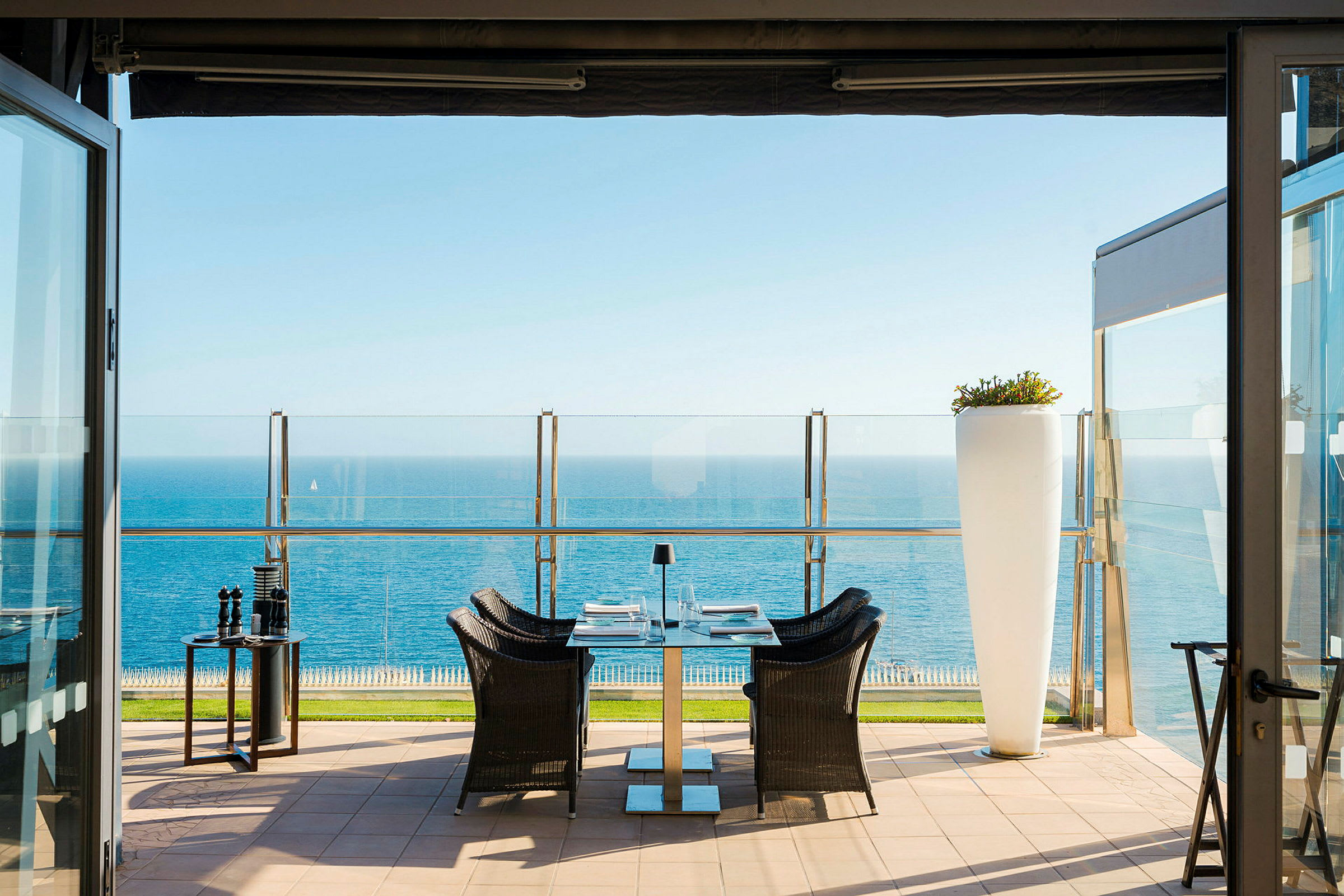 Terrasse med bord, stole og udsigt over havet. (AI-genereret tekst)