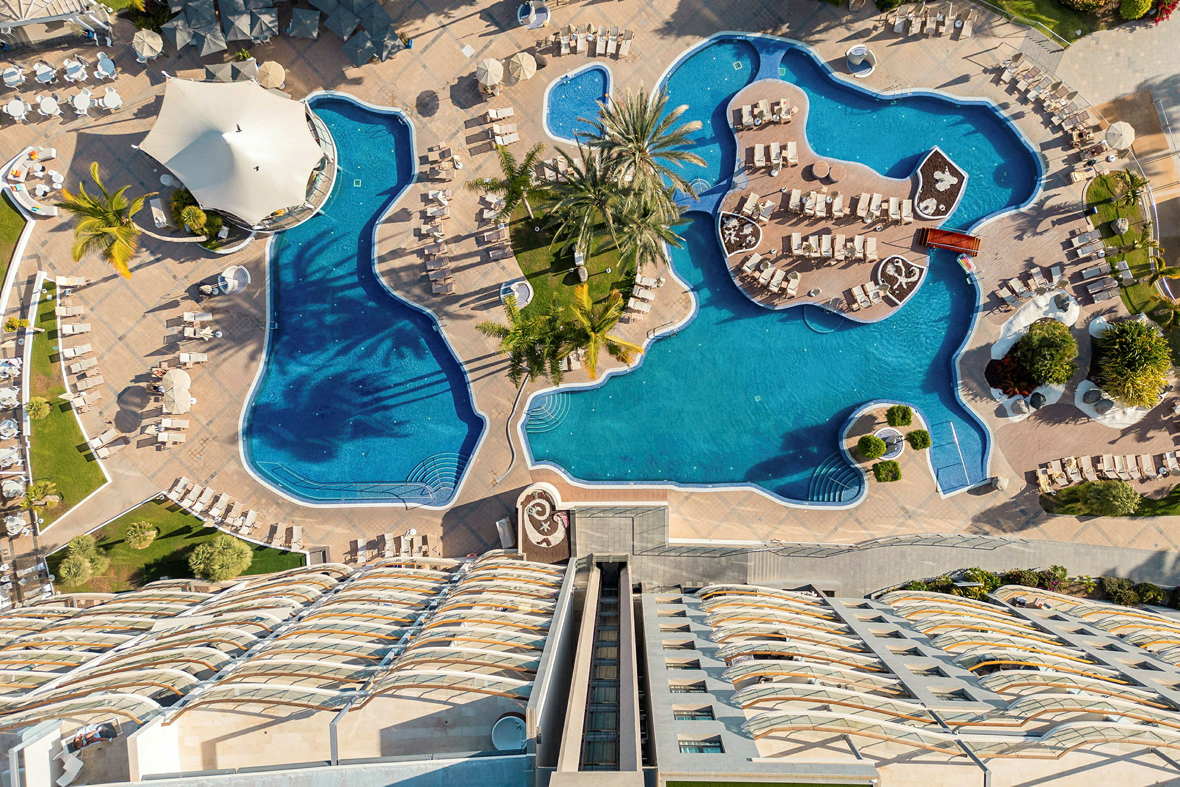 Et oversigtsbillede af en udendørs pool med liggestole og parasoller ved et hotel. (AI-genereret tekst)