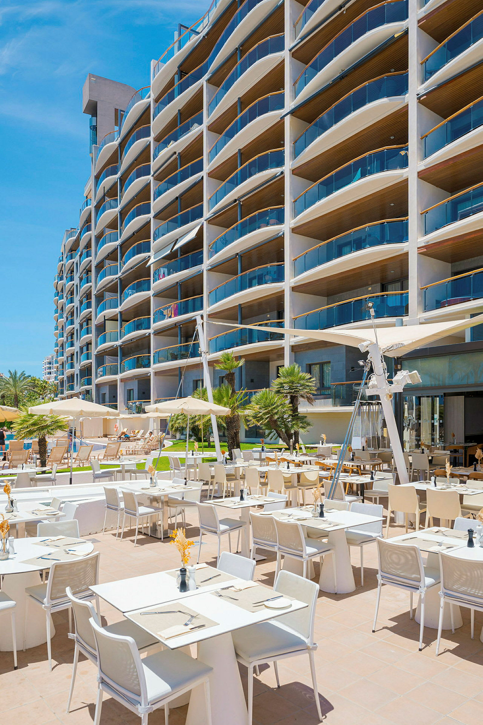 En udendørsrestaurant ved et moderne hotel med mange altaner. (AI-genereret tekst)