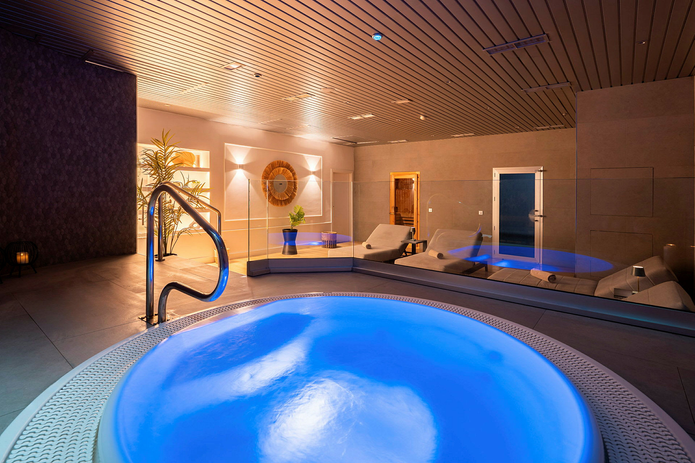 Interiør af et spa med en oplyst jacuzzi og liggestole. (AI-genereret tekst)