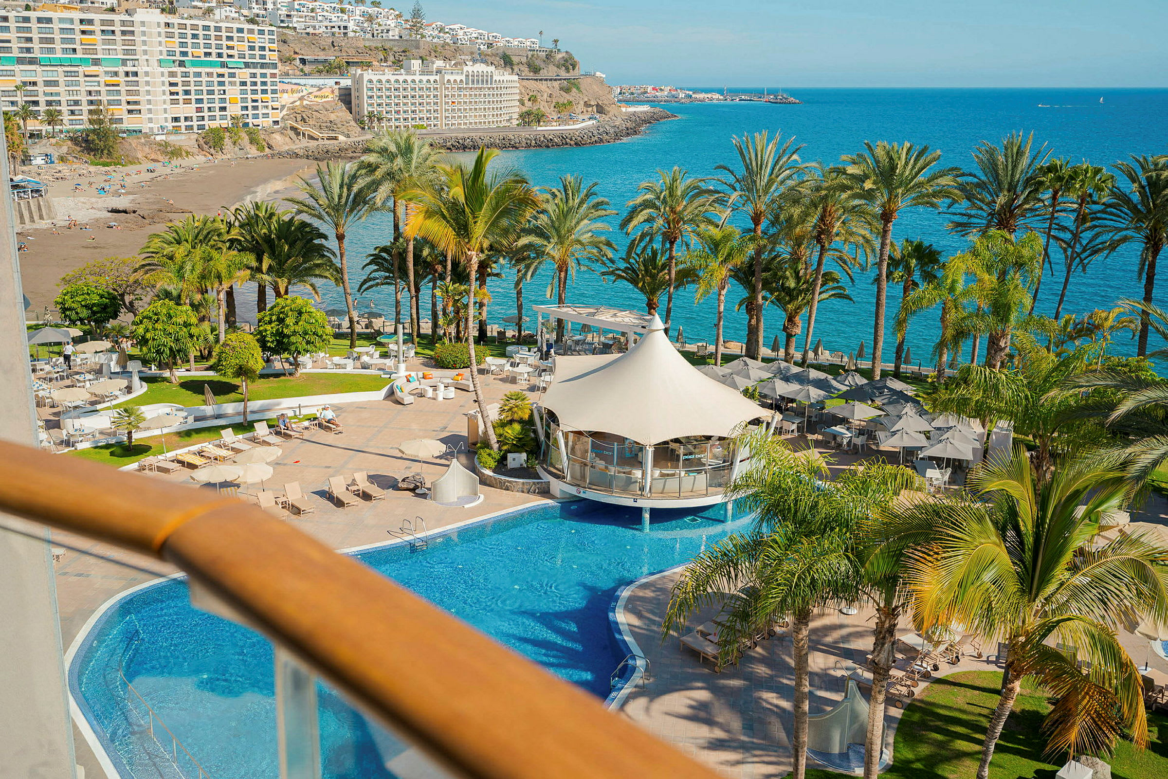 Billede af et resort med swimmingpool, liggestole, palmer og hav i baggrunden. (AI-genereret tekst)