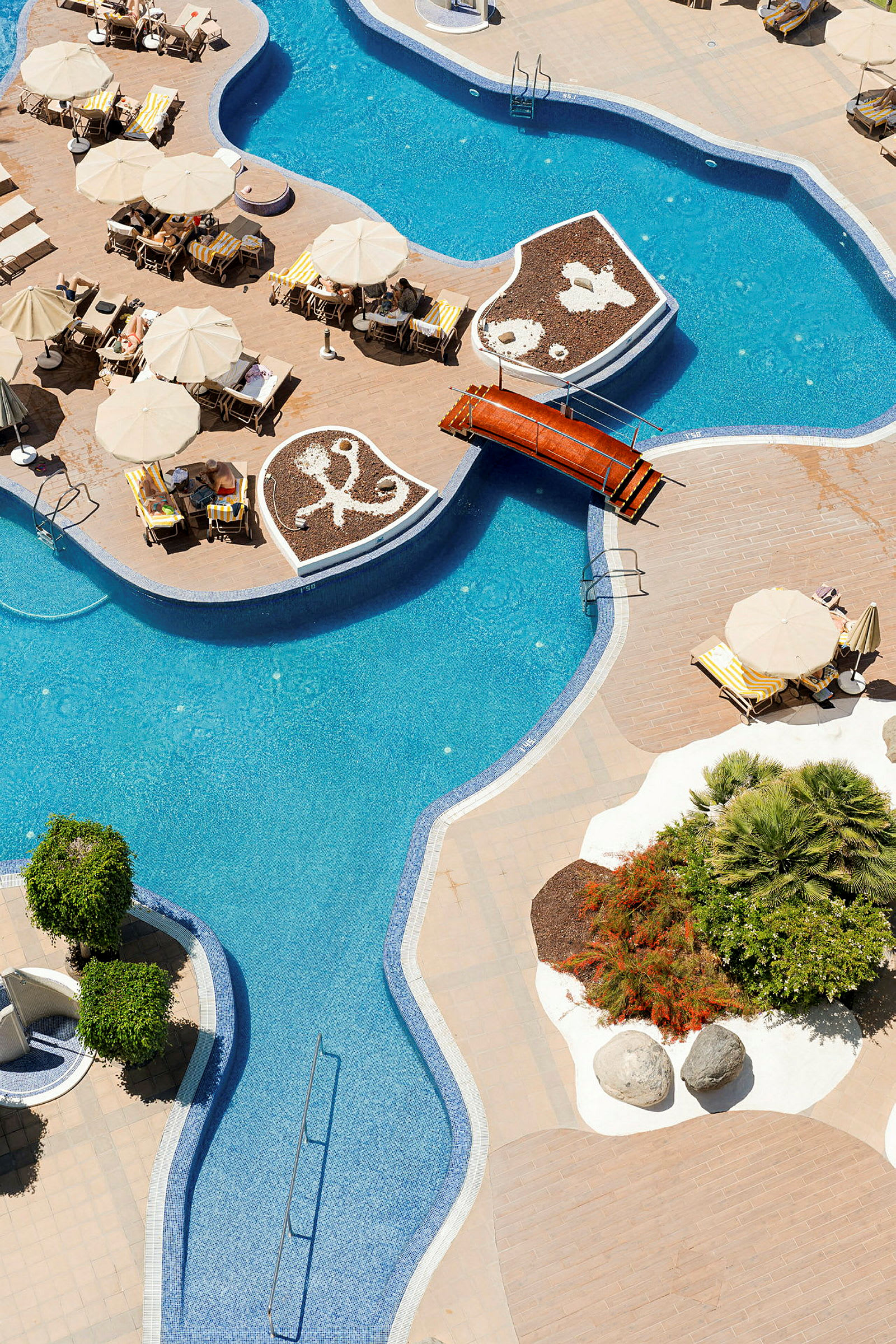 Billede af en snoet swimmingpool med liggestole og parasoller ved siden af, samt dekorative beplantninger og gangbro. (AI-genereret tekst)
