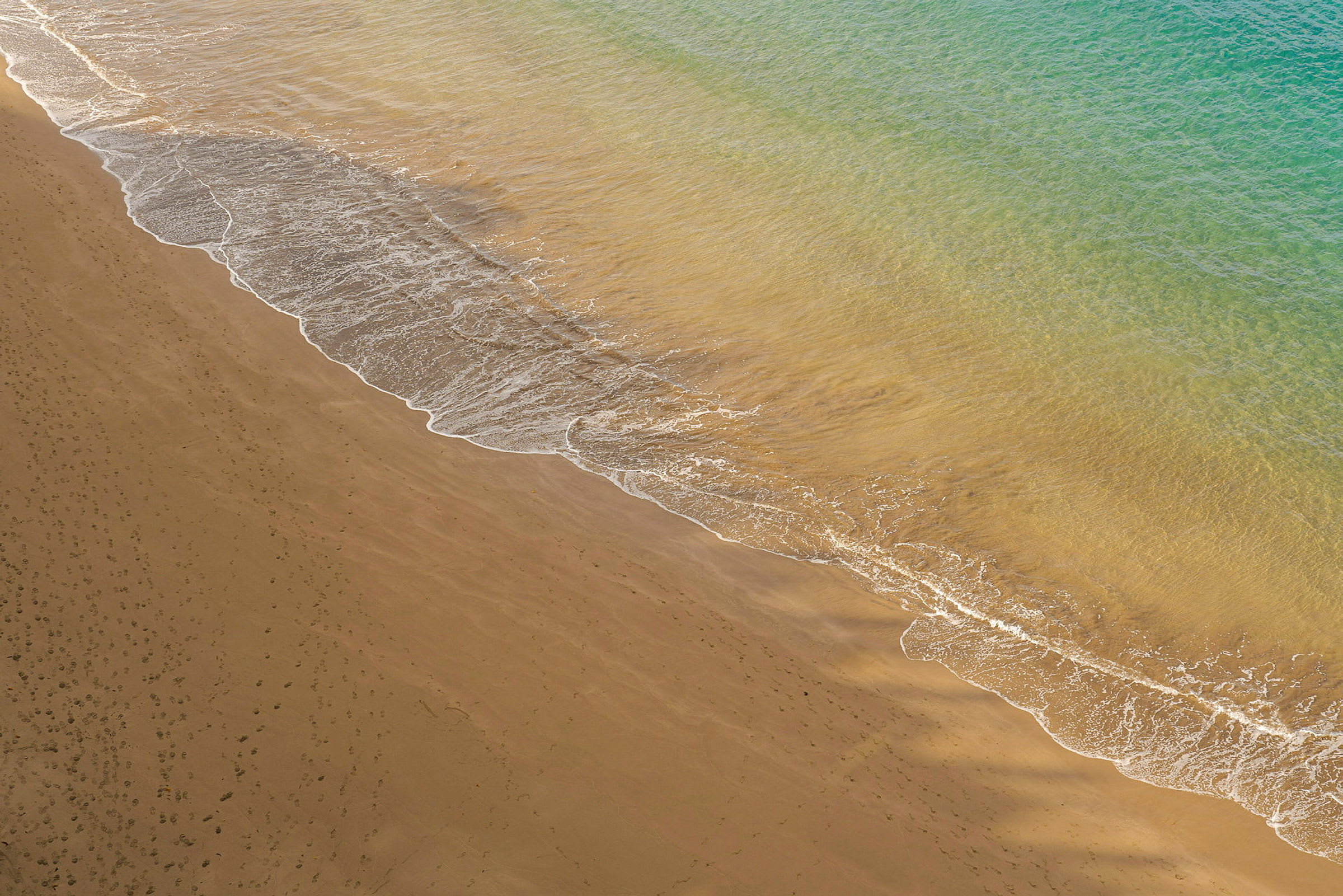 Billedet viser en sandstrand med bølger fra havet, der når kanten. (AI-genereret tekst)