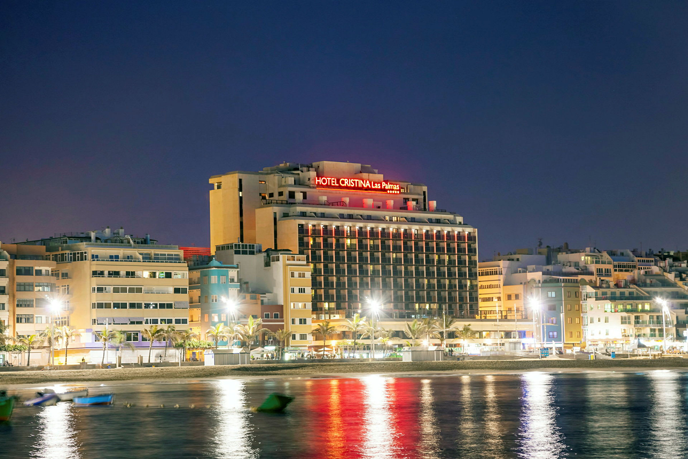 Billede af hotelbygning med neonlys i nattemiljø, beliggende tæt på vand. (AI-genereret tekst)