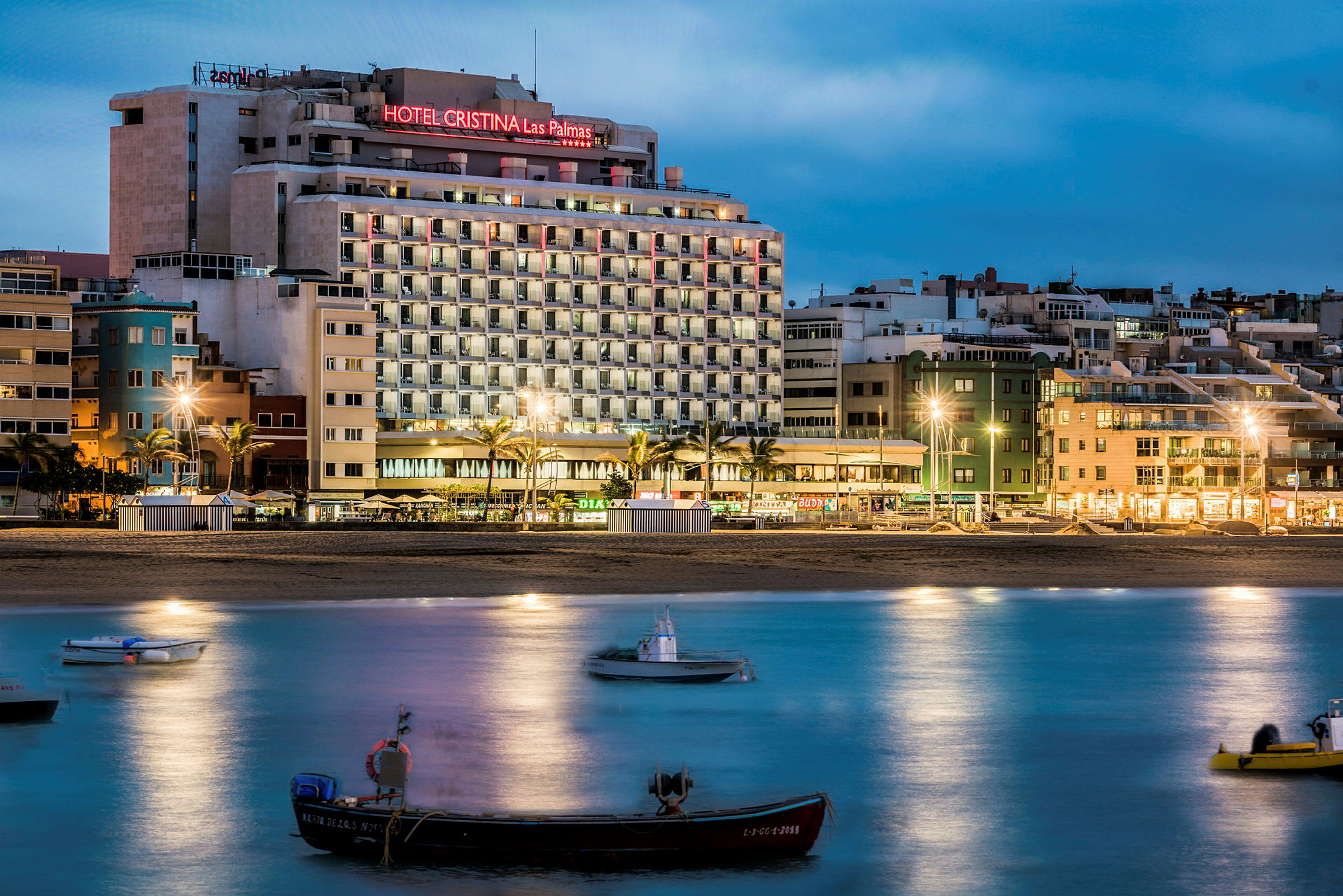 Hotelbygning nær strand, både på vandet i forgrunden. (AI-genereret tekst)