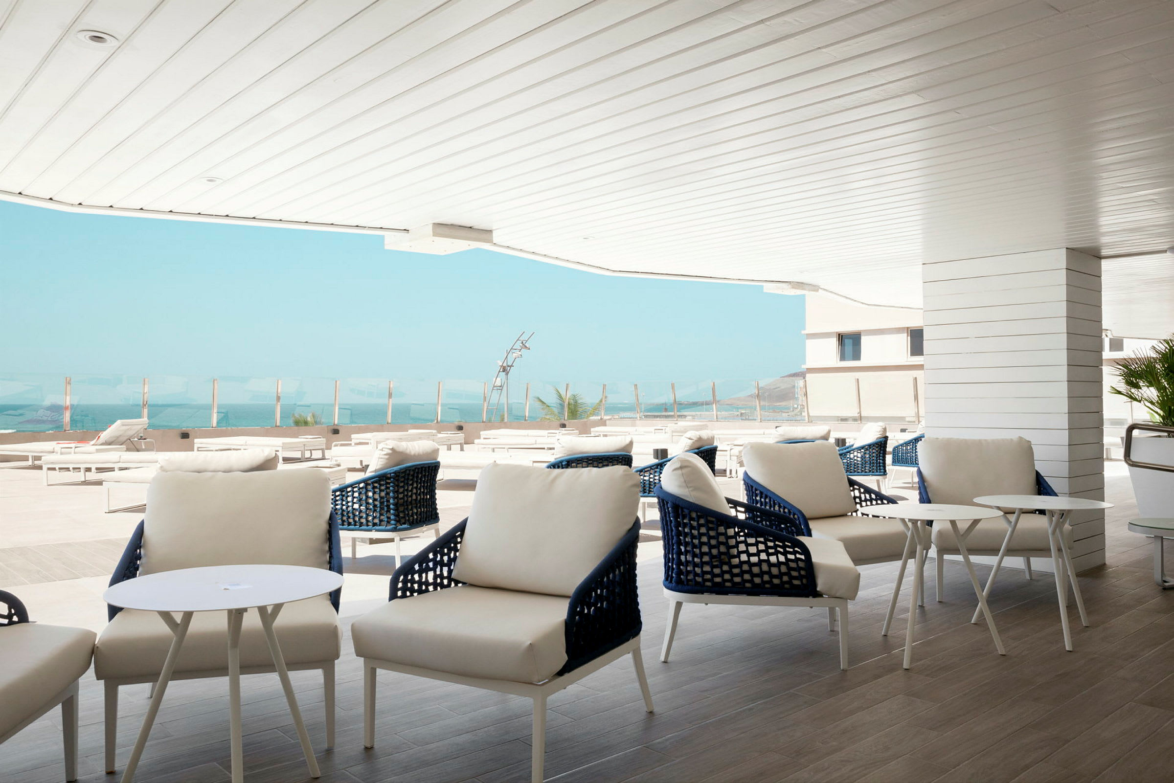 Moderne udendørs lounge med hvide møbler og udsigt over havet. (AI-genereret tekst)